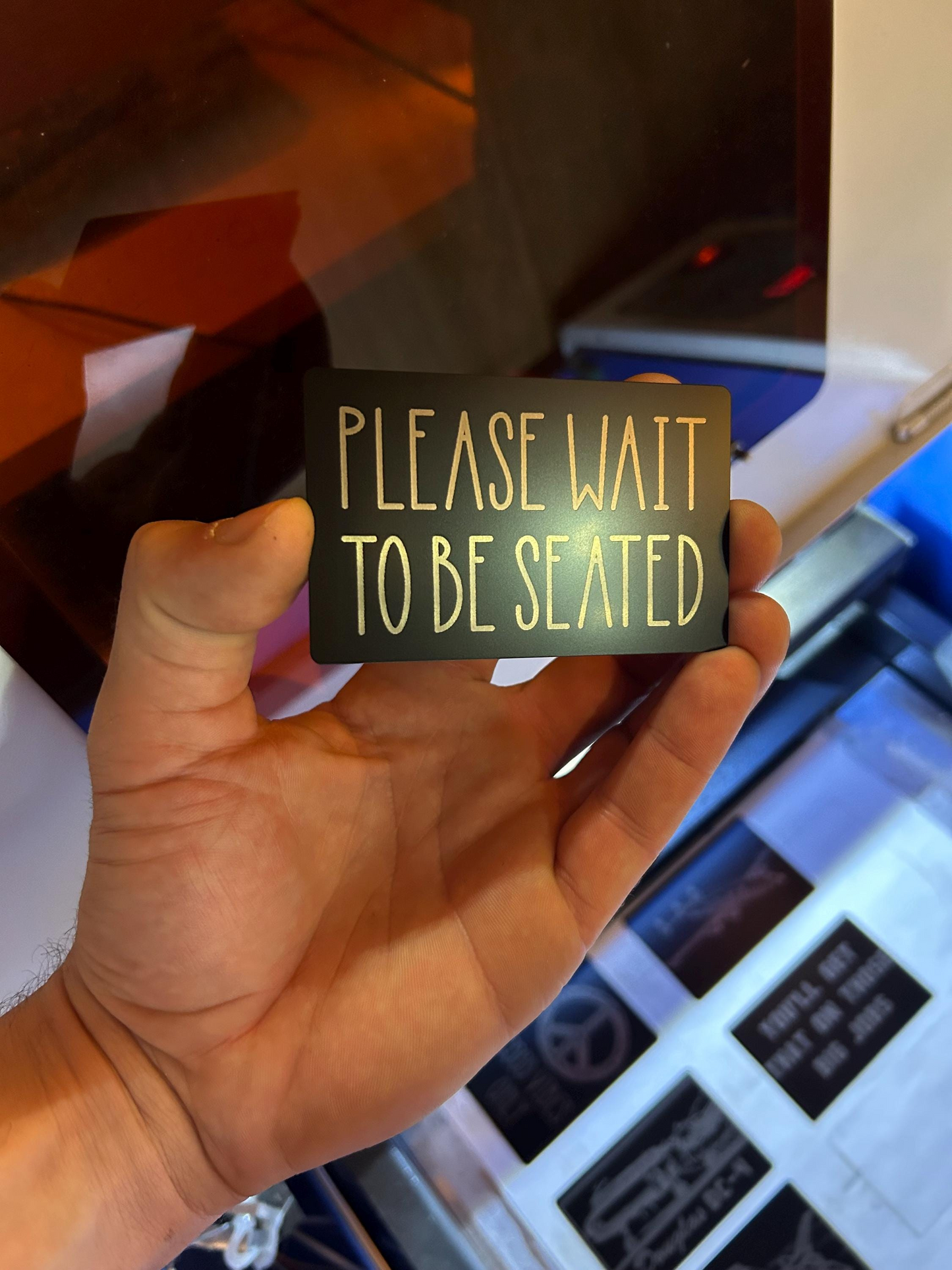Hand holding a sign that says 'Please wait to be seated' with a blurred background.