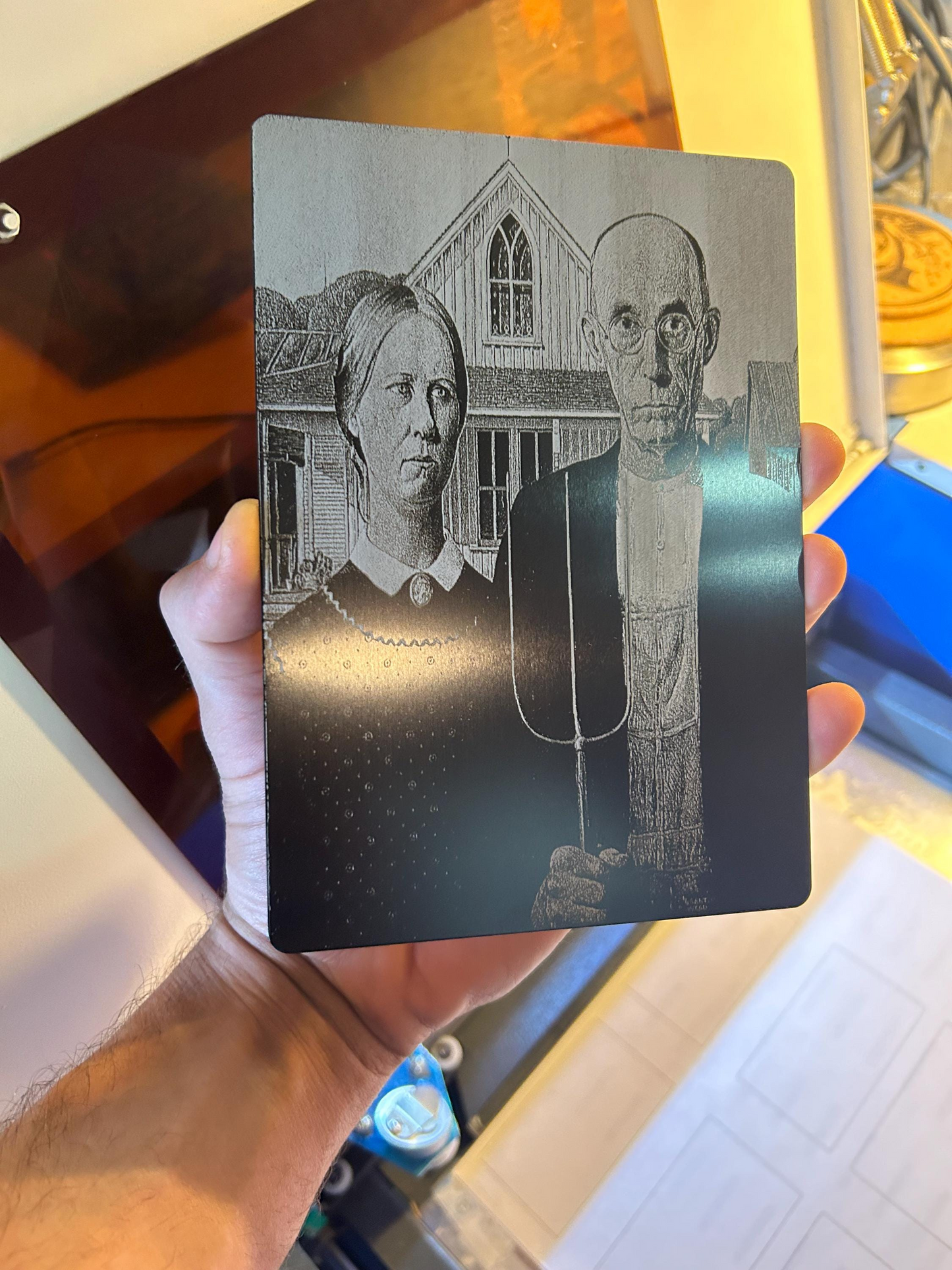 Hand holding decorative plaque with laser engraved American Gothic classic american folklore painting design