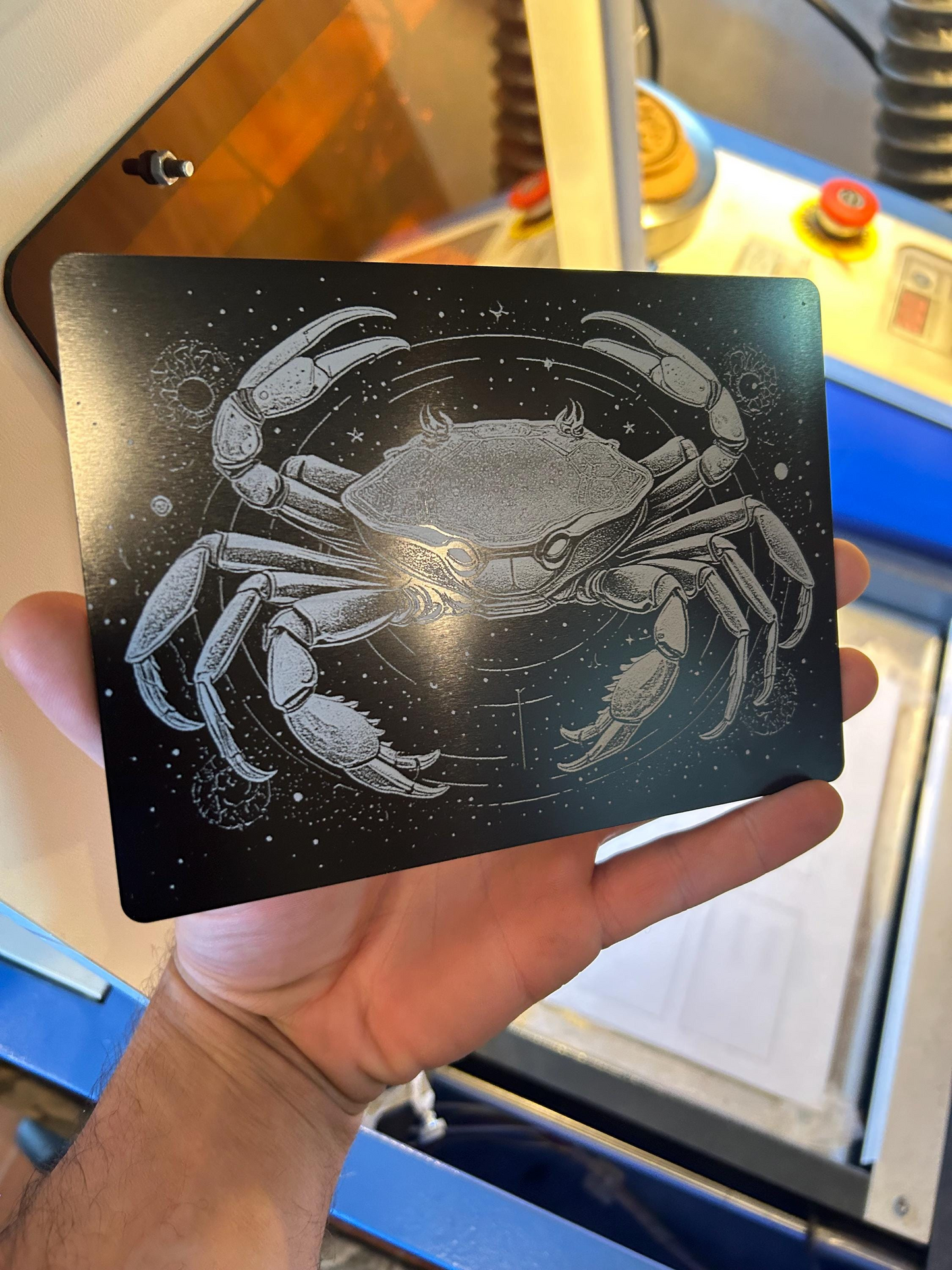 Hand holding a metal laser engraved decorative plaque with a cancer crab design against a blurred background
