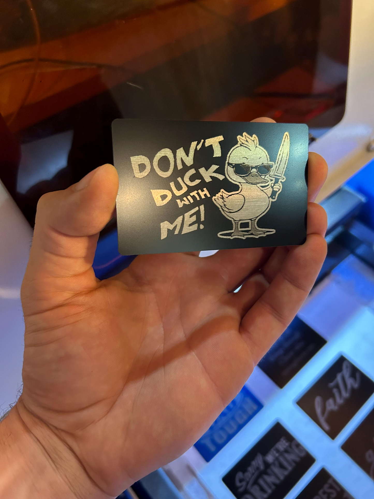 Angled shot of custom black/silver anodized aluminum joke card – duckling illustration and bold “DON’T DUCK WITH ME” typography