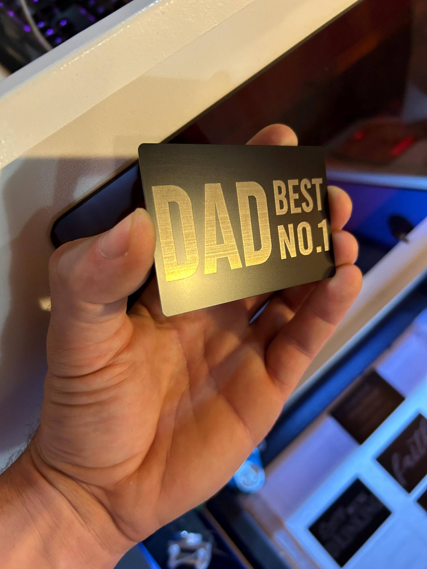 Hand holding a metal keepsake card with 'DAD BEST NO.1' text in silver on a metal business card
