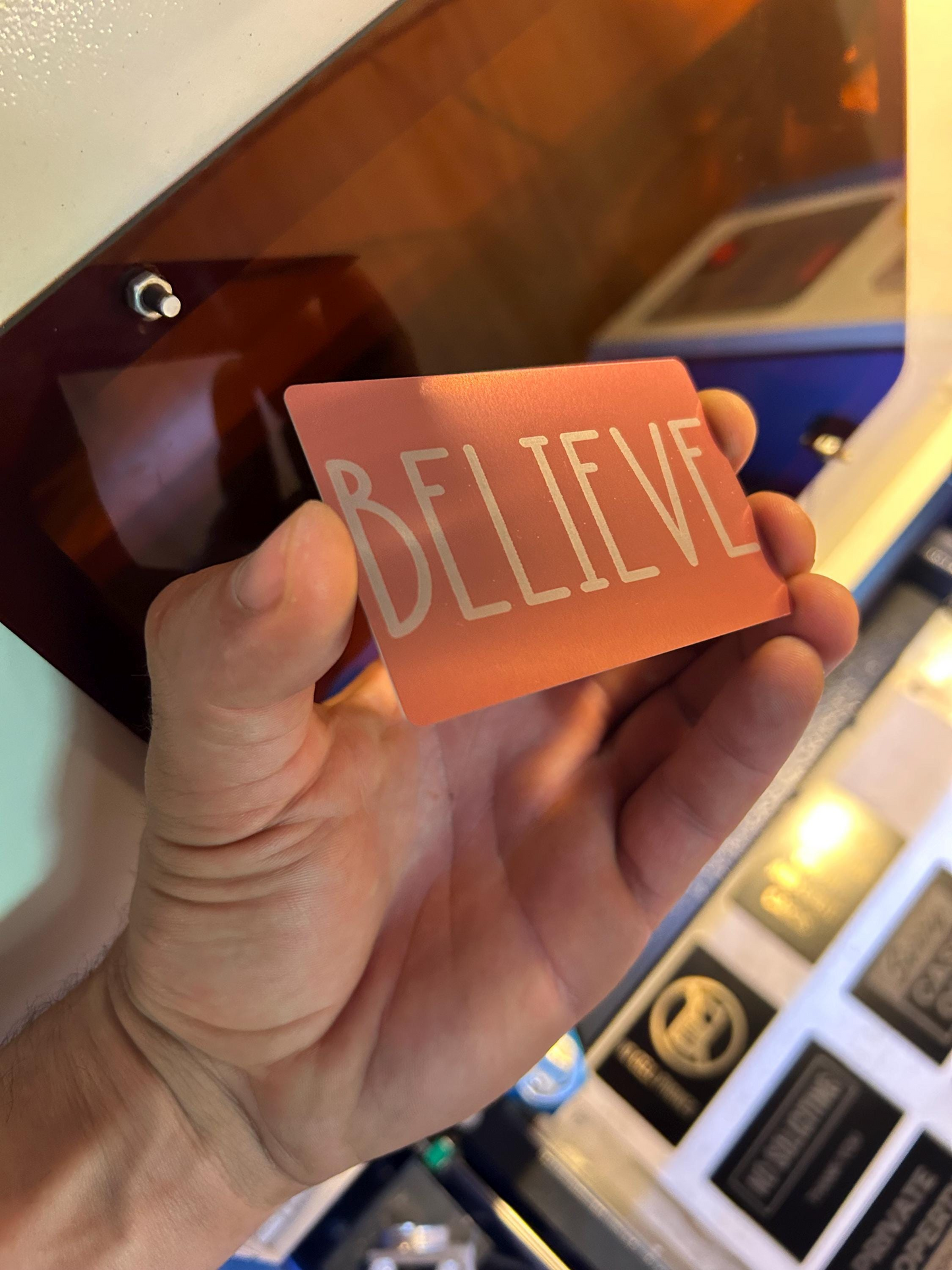 Angled shot of laser engraved rose gold keepsake card featuring “BELIEVE” typography design