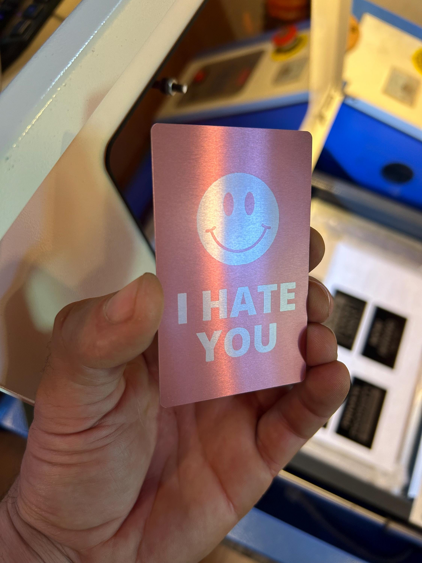 Hand holding custom metal business card in rose gold/silver with "I hate you" and a cute smiley face