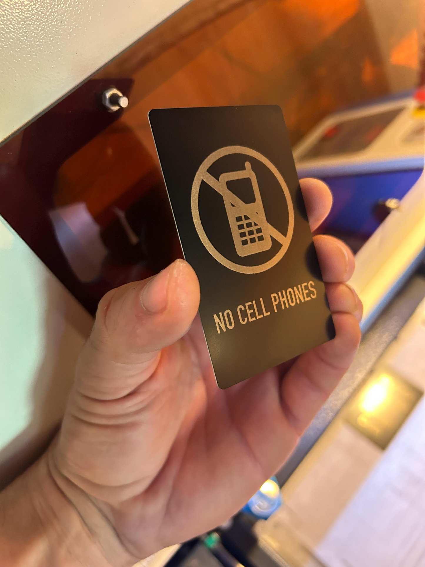 Hand holding a 'No Cell Phones' placard in front of a blurred background