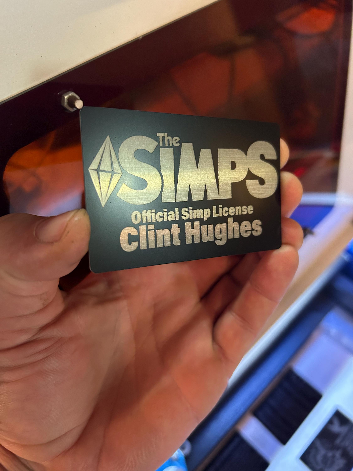 Hand holding a 'The Simps' license gag gift card with custom name engraving