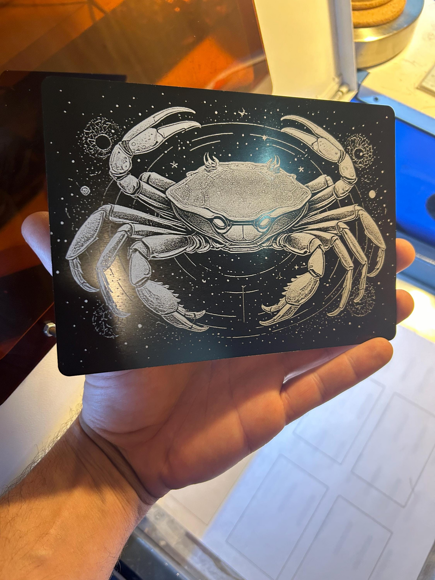 Hand holding a laser engraved decorative plaque with a detailed zodiac spiritual illustration of a crab against a starry background.