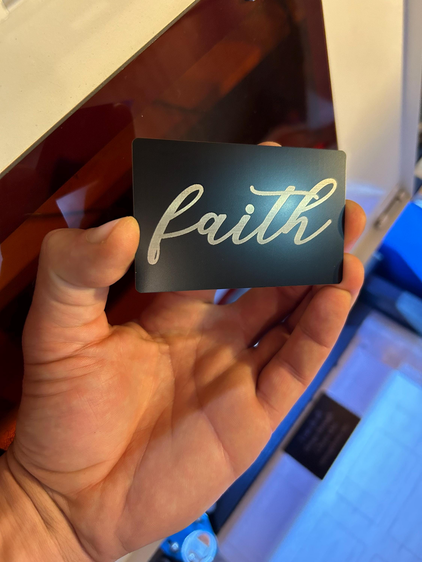 Hand showcasing a laser engraved religious keepsake card with elegant “Faith” script text