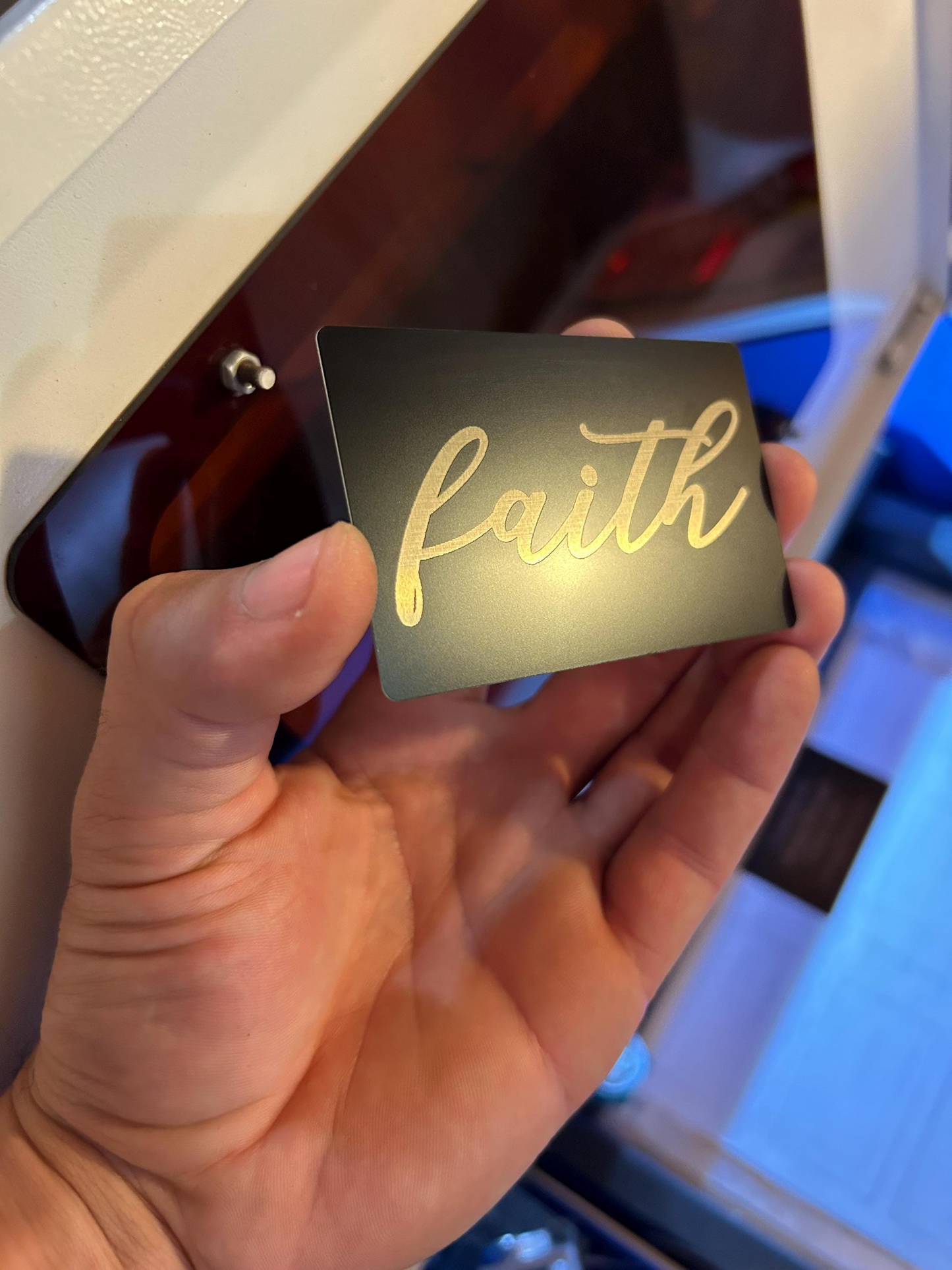 Hand presenting a faith-inspired engraved metal card with cursive typography design that reads: Faith