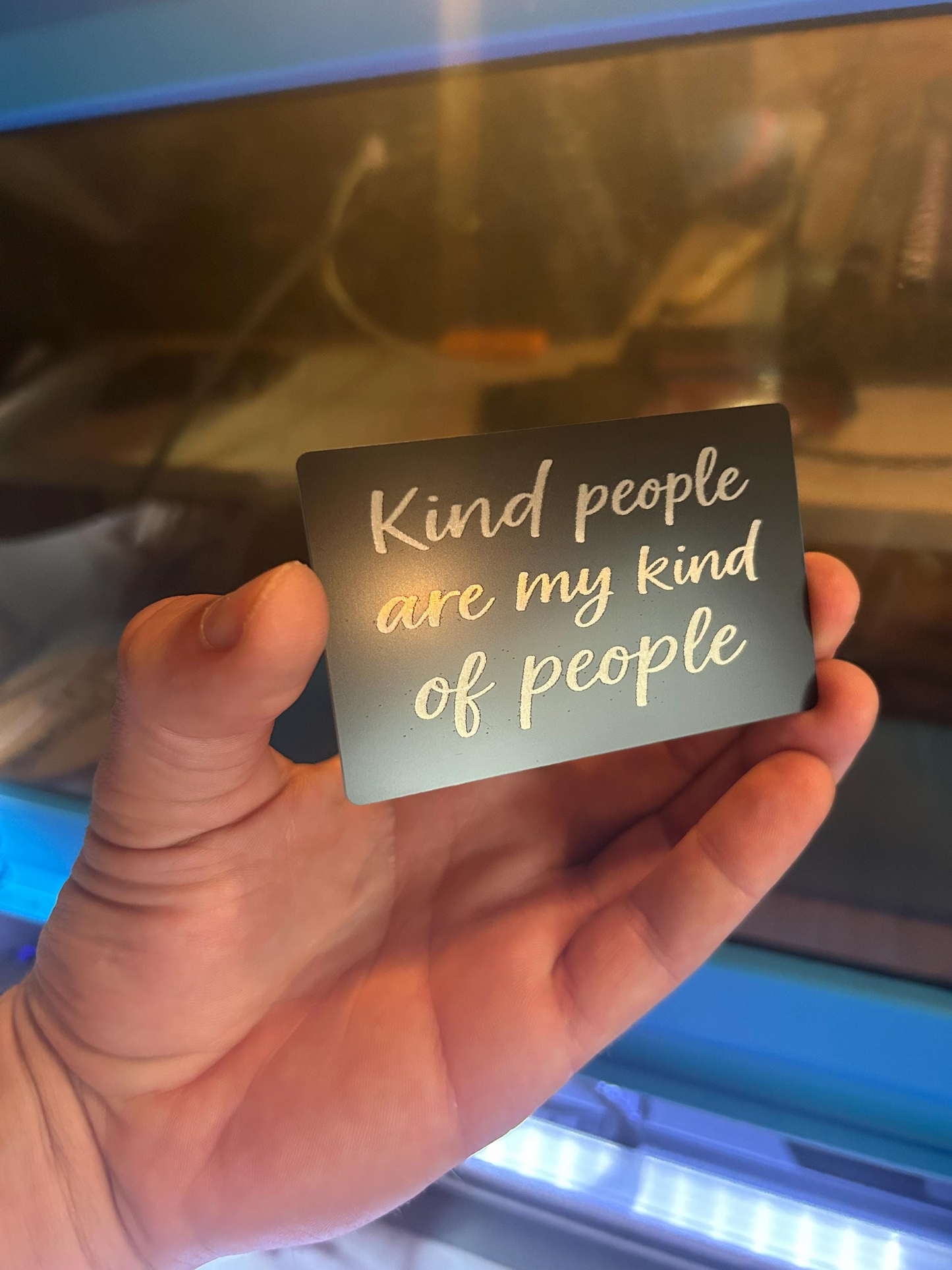 Hand holding a laser engraved anodized aluminum keepsake card with 'Kind people are my kind of people' text.