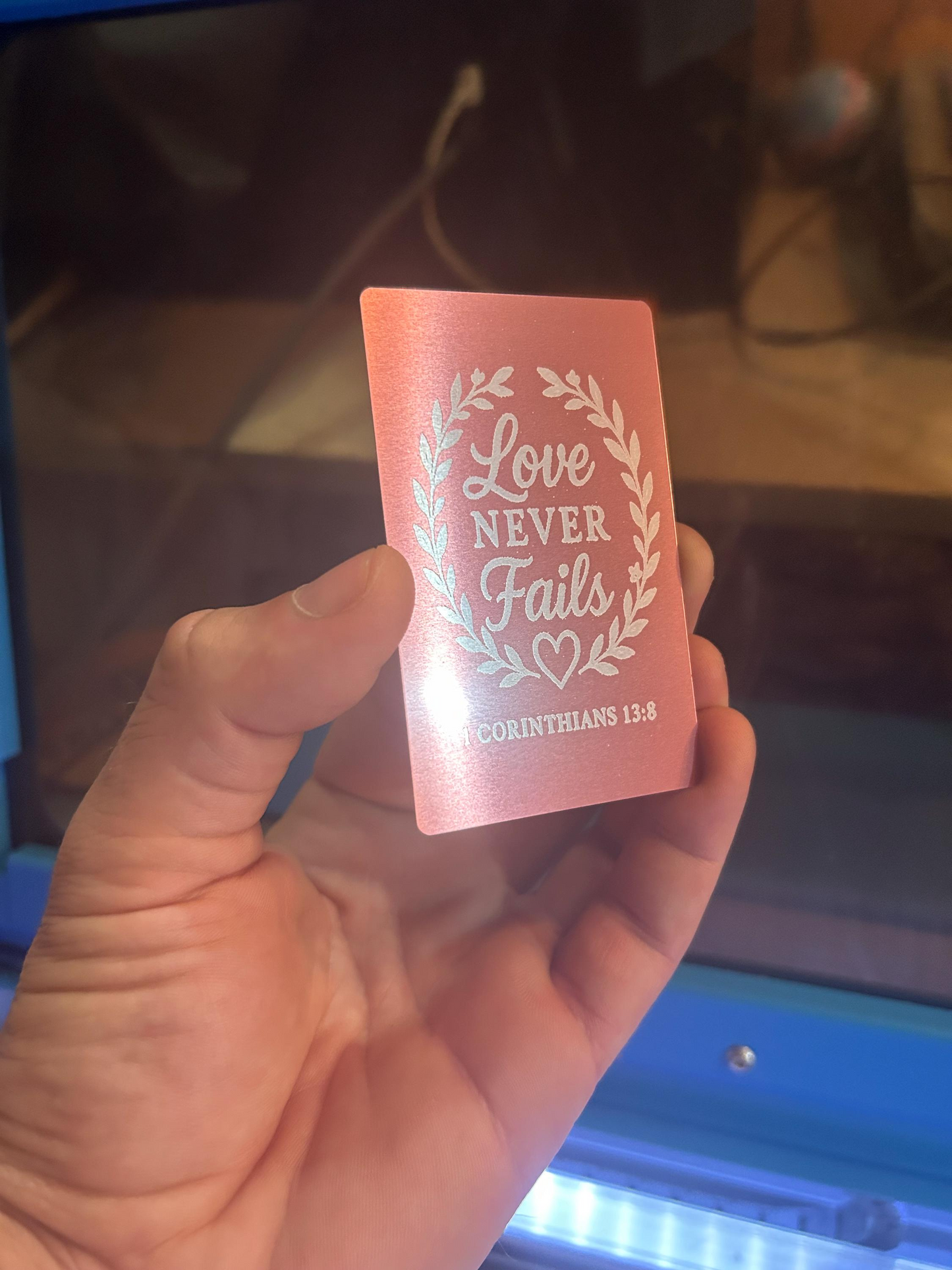 Detailed shot of rose gold anodized metal scripture card engraved with “Love Never Fails” and 1 Corinthians 13:8