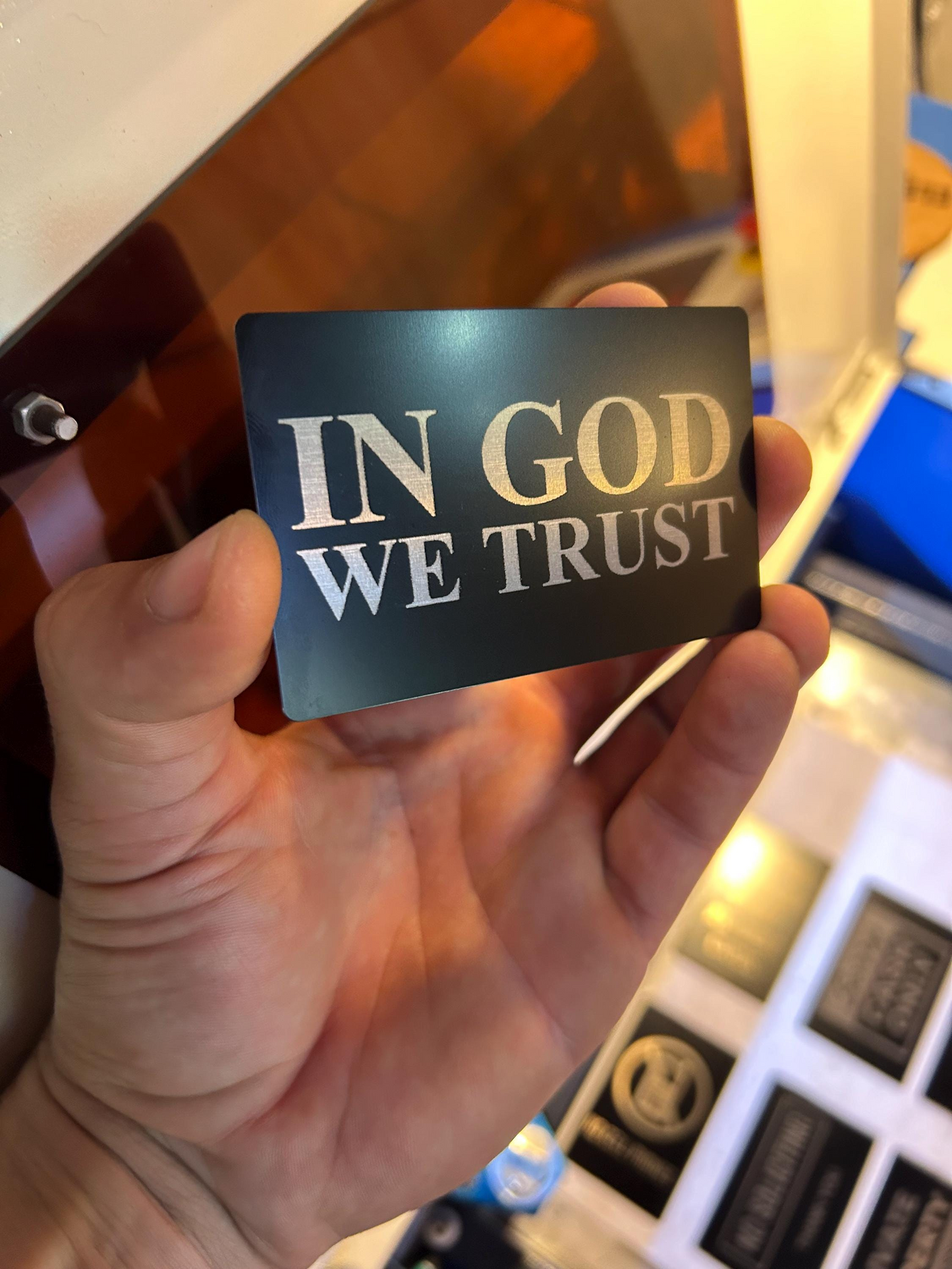 Hand holding a laser engraved placard with 'IN GOD WE TRUST' text laser engraved
