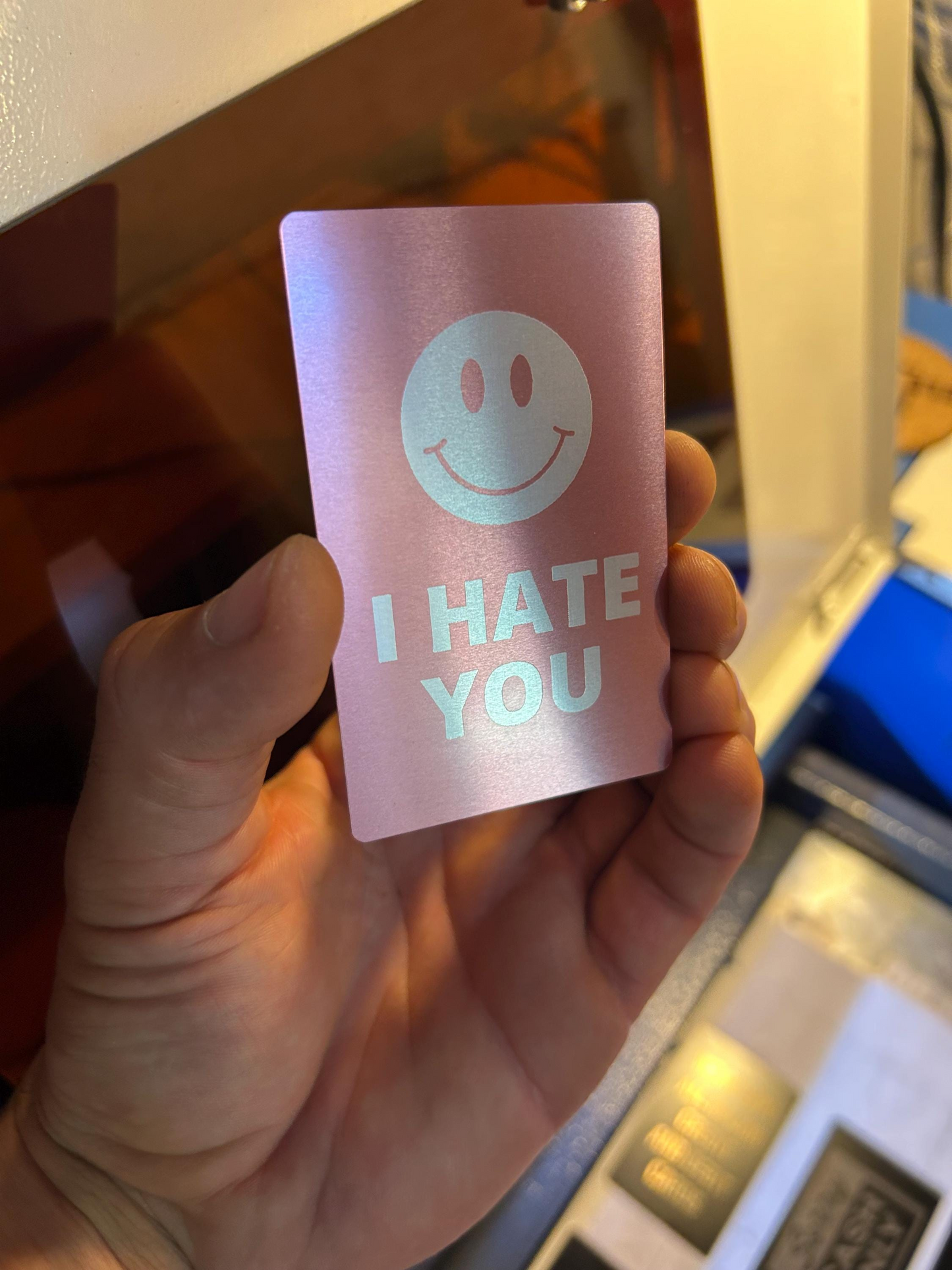 Hand holding a pink card with a smiley face and 'I HATE YOU' text.