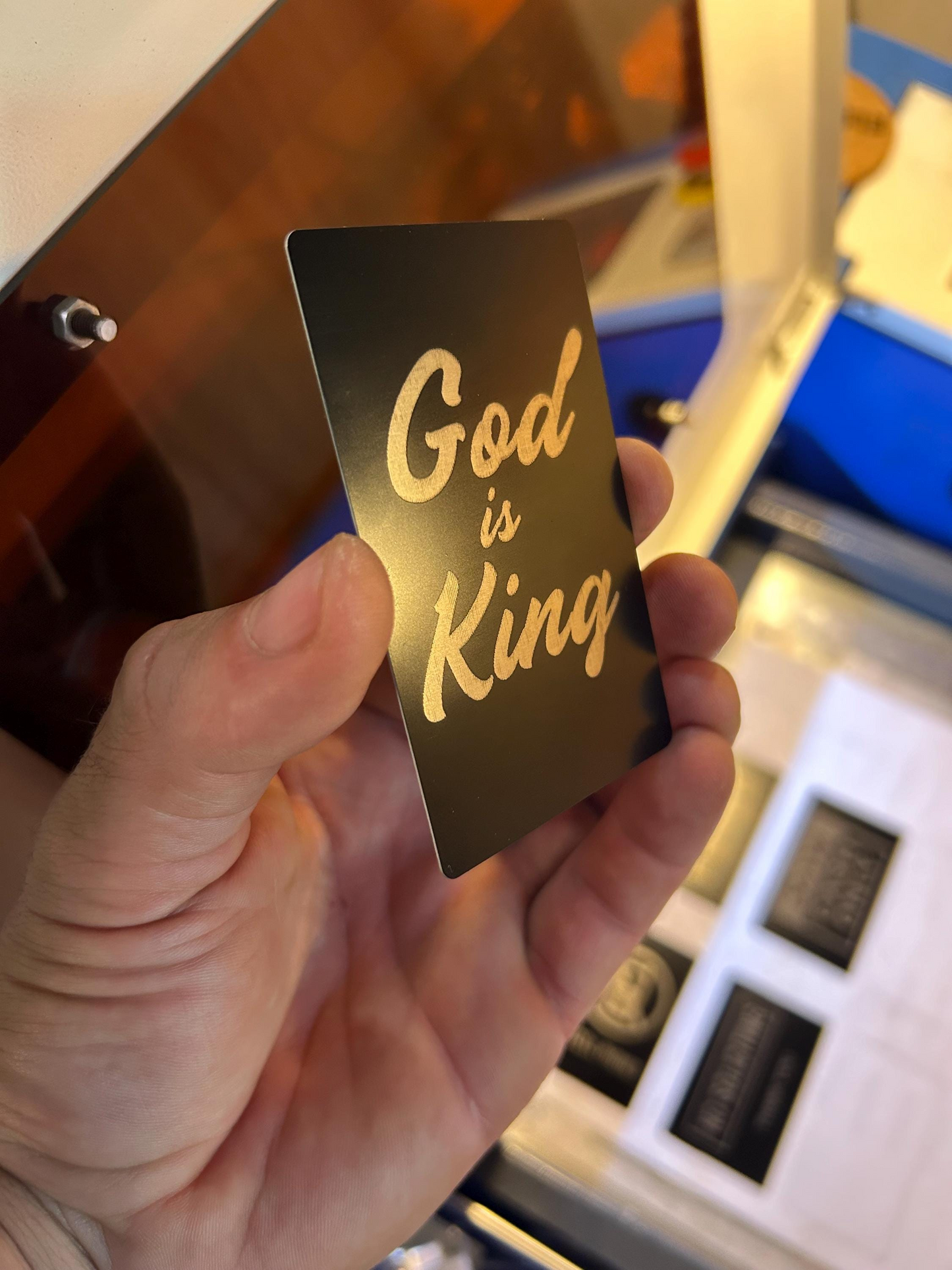 Hand holding a metal faith inspired gift card with 'God is King' in silver text against a blurred background.