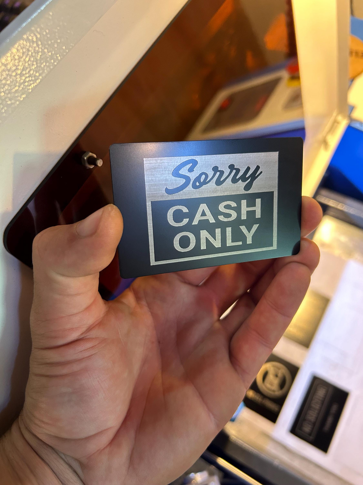 Hand holding a 'Sorry Cash Only' sign in front of a cash machine.