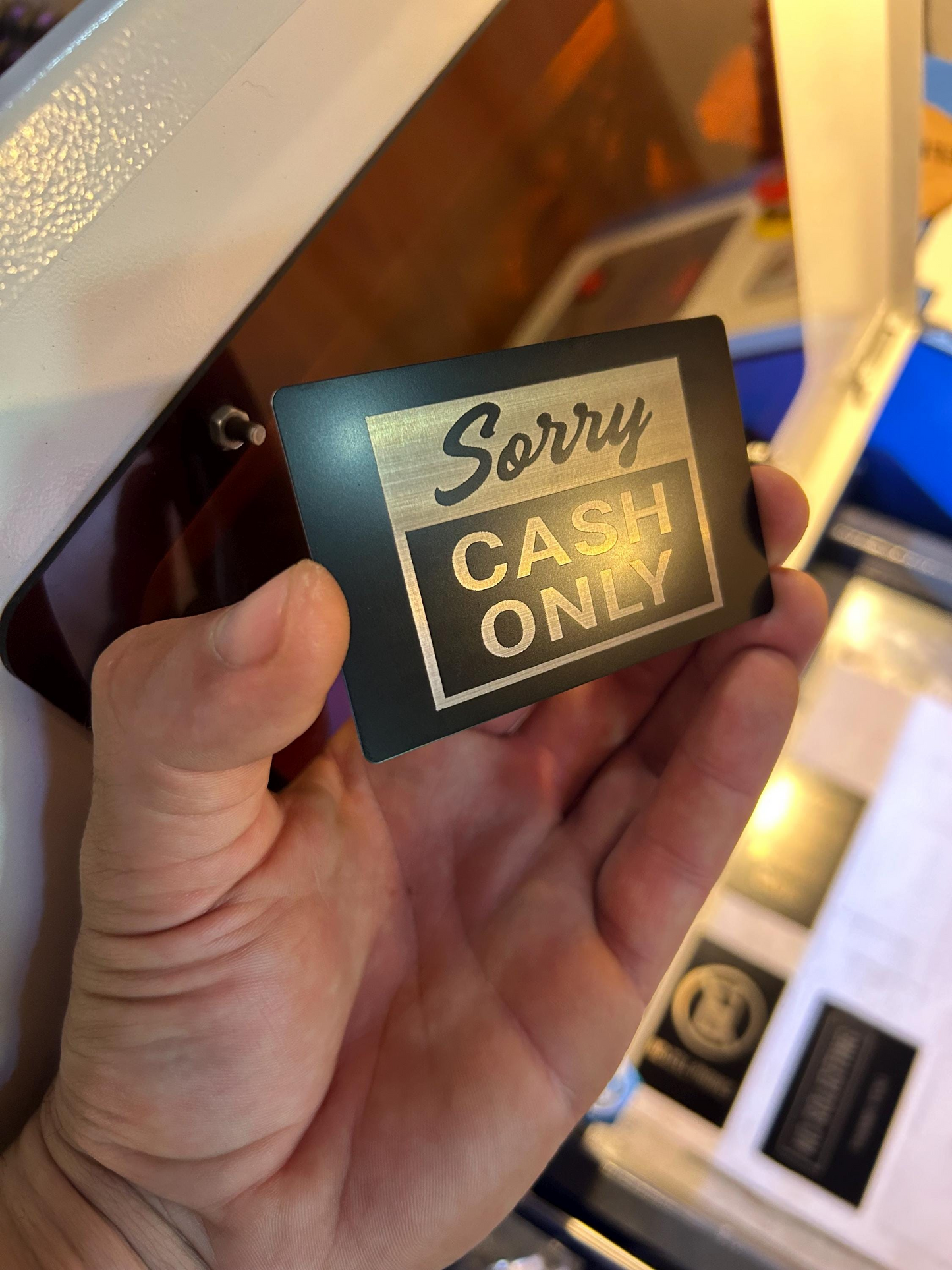 Hand holding a sign that says 'Sorry Cash Only' in front of a cash machine.