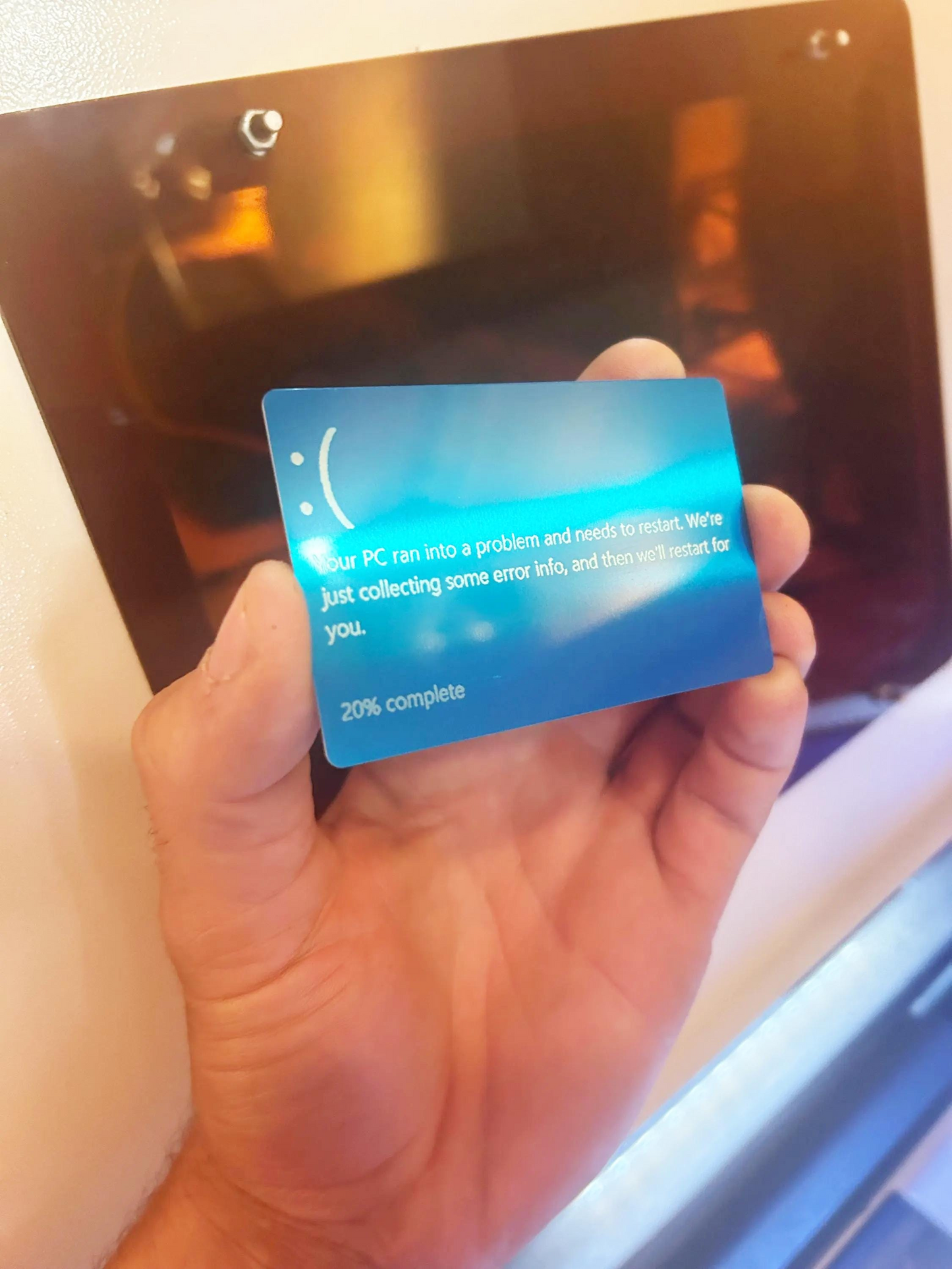 Hand holding a metal blue novelty gift card with screen error card with laser engraved text in front of a computer screen