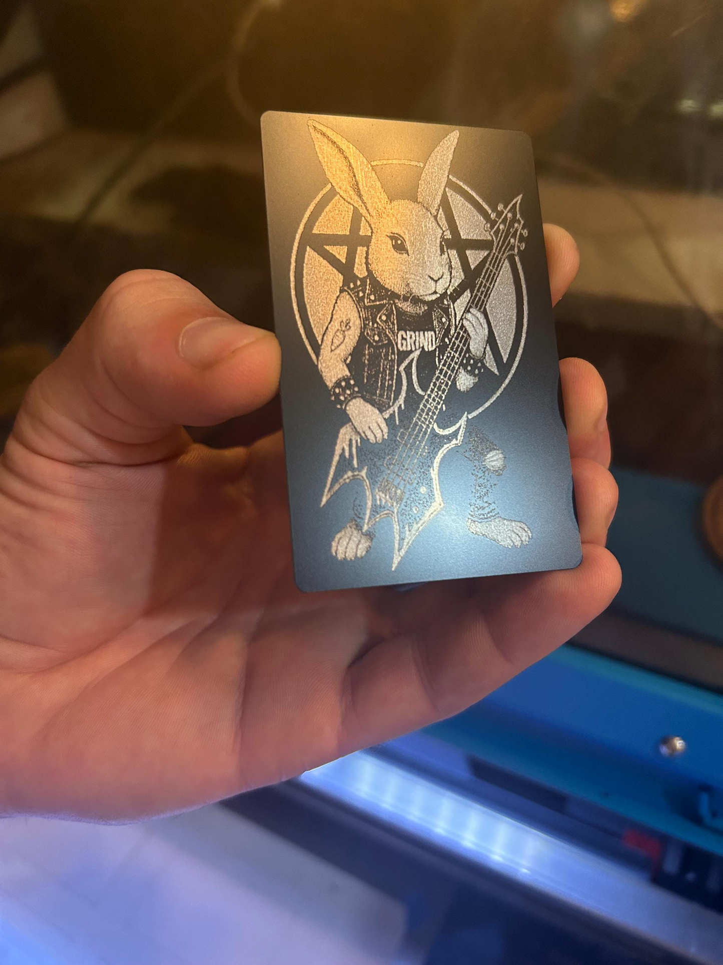 Hand holding a laser engraved metal keepsake card with black/silver illustration art of heavy metal rocker bunny with bass guitar
