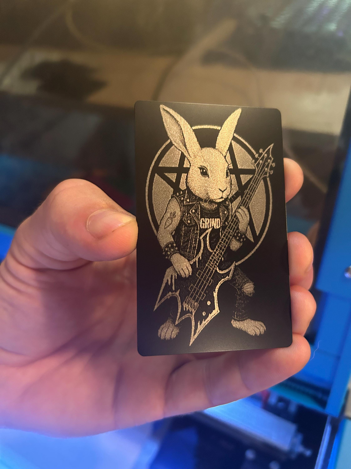 Hand holding a laser engraved anodized aluminum wallet insert card, with funny hardcore punk heavy metal rocker bassist rabbit illustration graphic