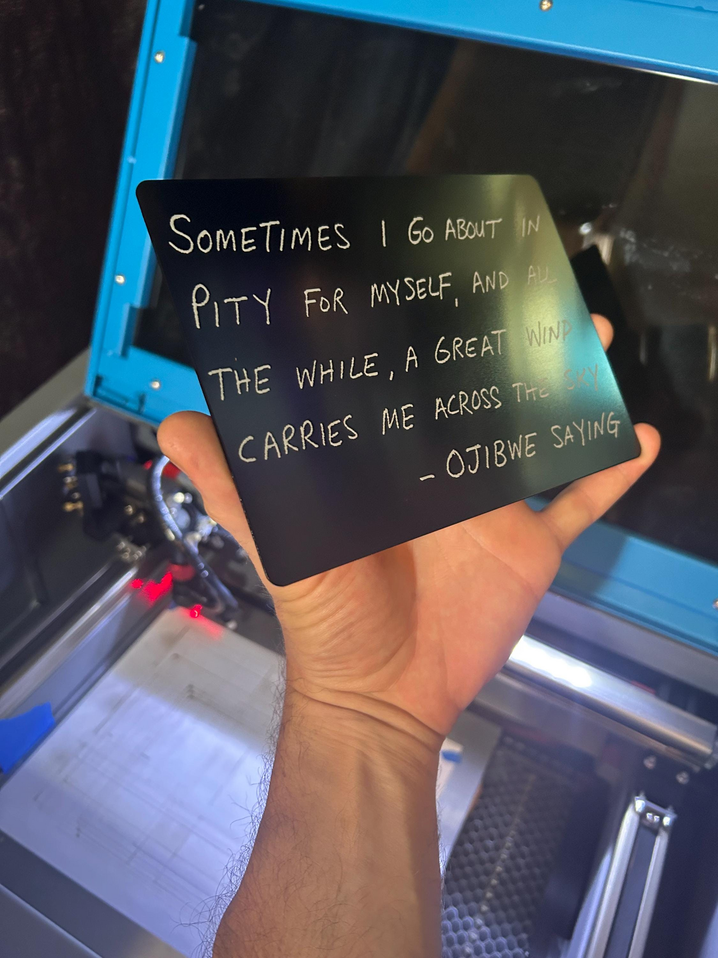 Hand holding laser engraved metal decorative placard with ojibwe inspirational quote on black/silver plaque