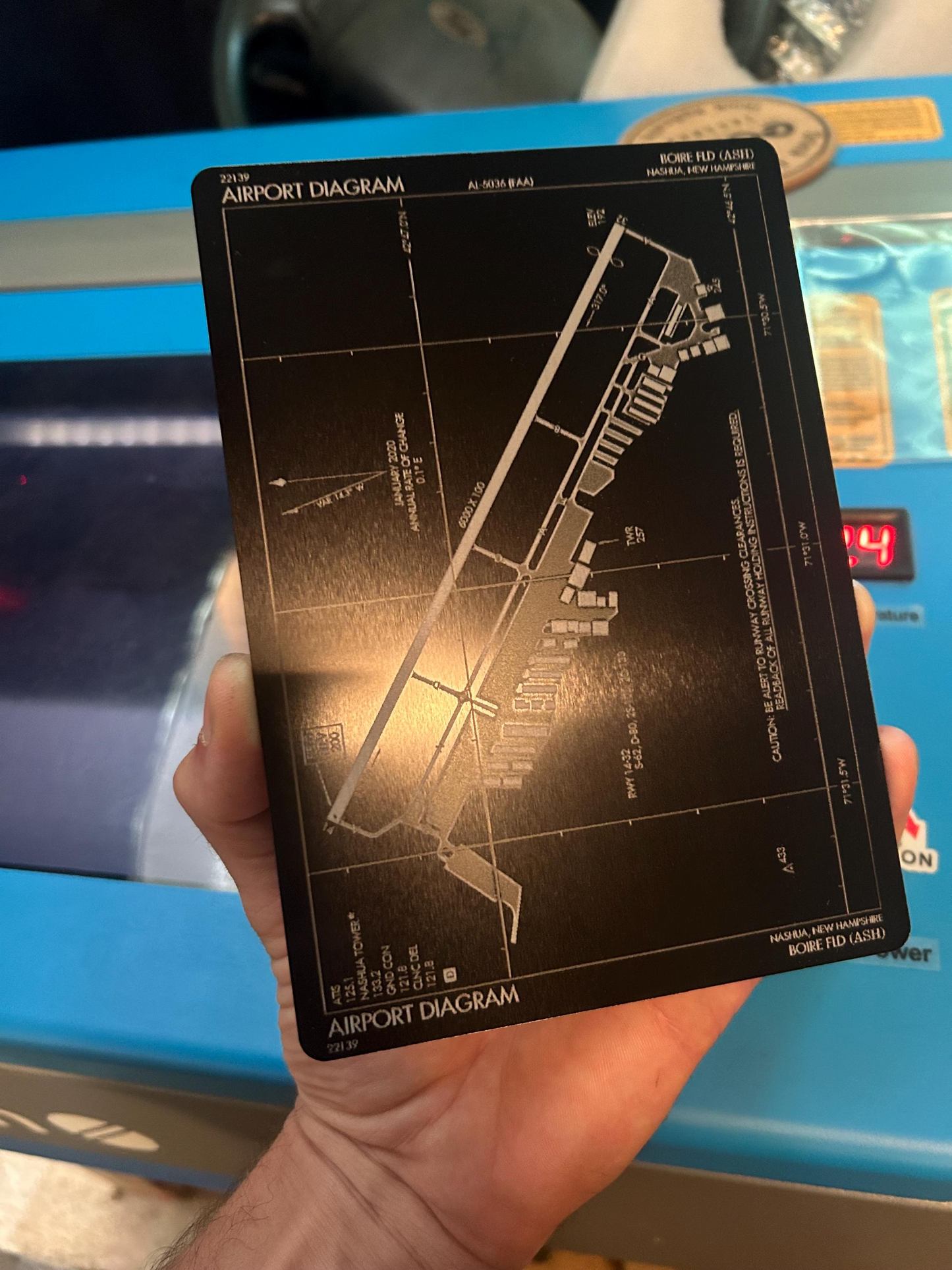 Hand holding a metal engraving with an airport diagram against a blurred background