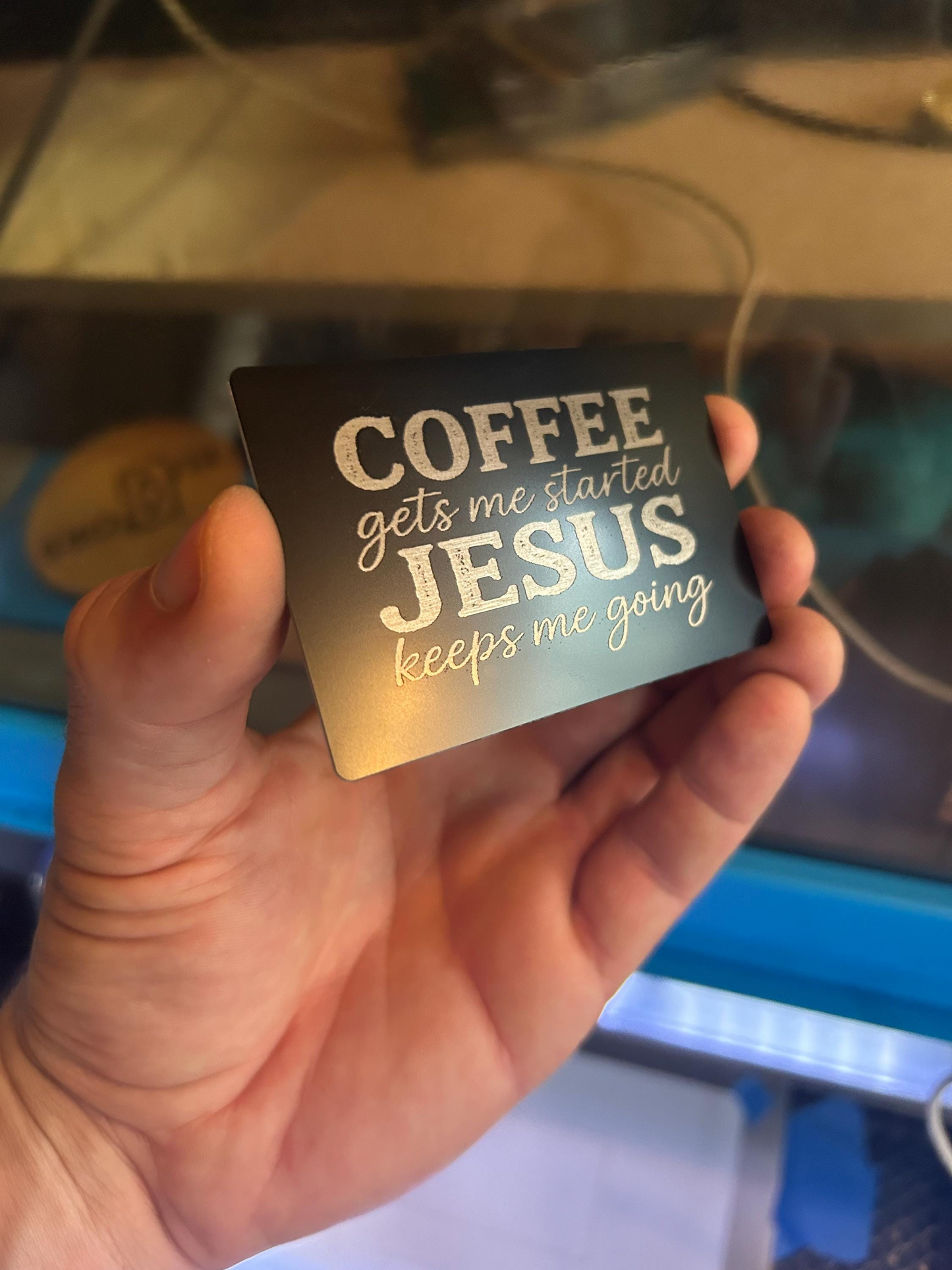 Human hand showcasing engraved Christian faith card with humorous inspirational text about coffee and Jesus