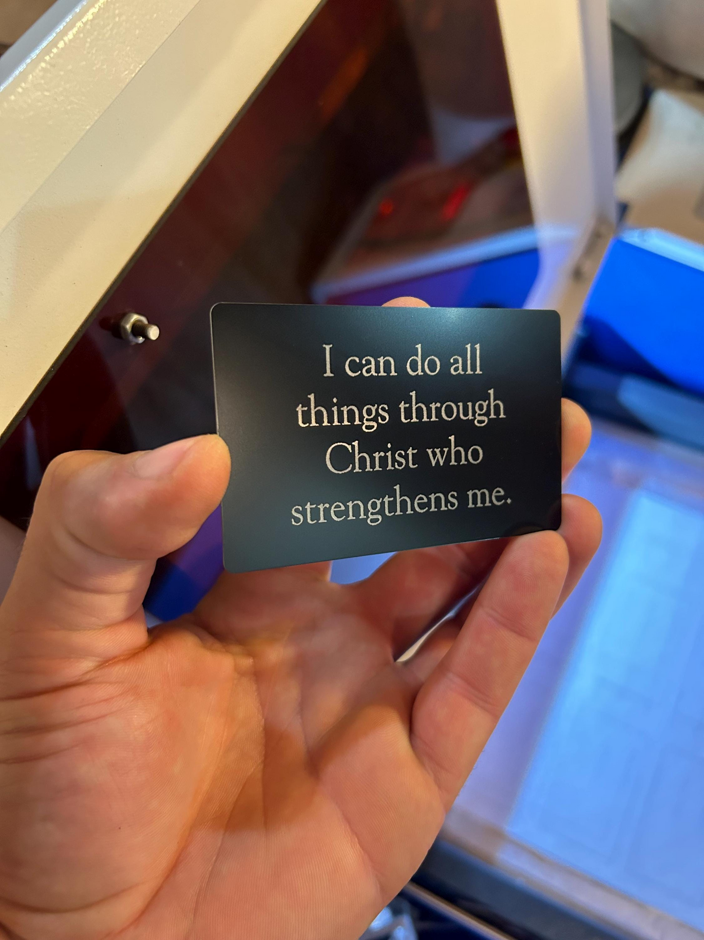 Hand holding a black card with "I Can Do ALL Things Through Jesus Christ" quote in front of a blurred background