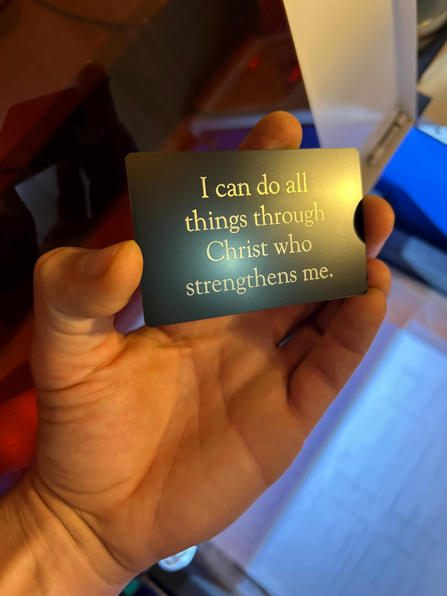 Hand holding a black/silver card with faith inspired christian scripture quote against a blurred background