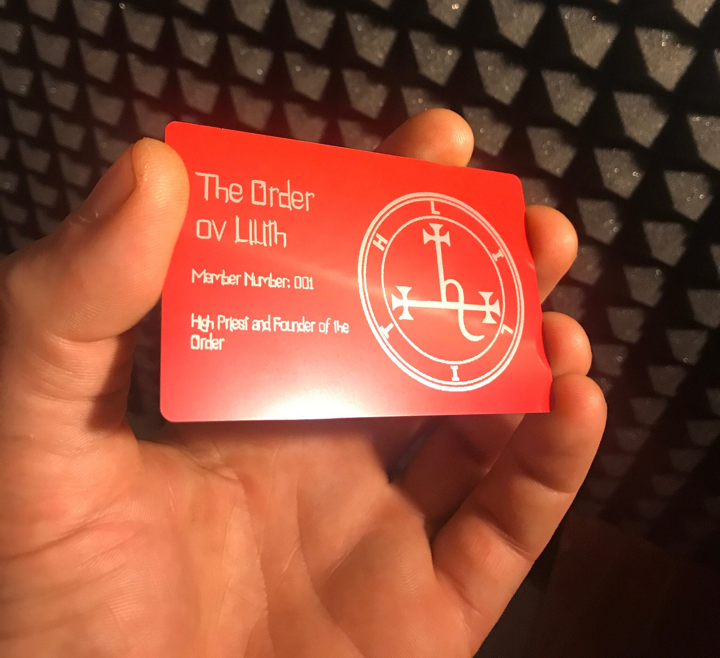 Red metal business card card with silver laser engraved text and custom logo symbol held by a hand against a textured black background
