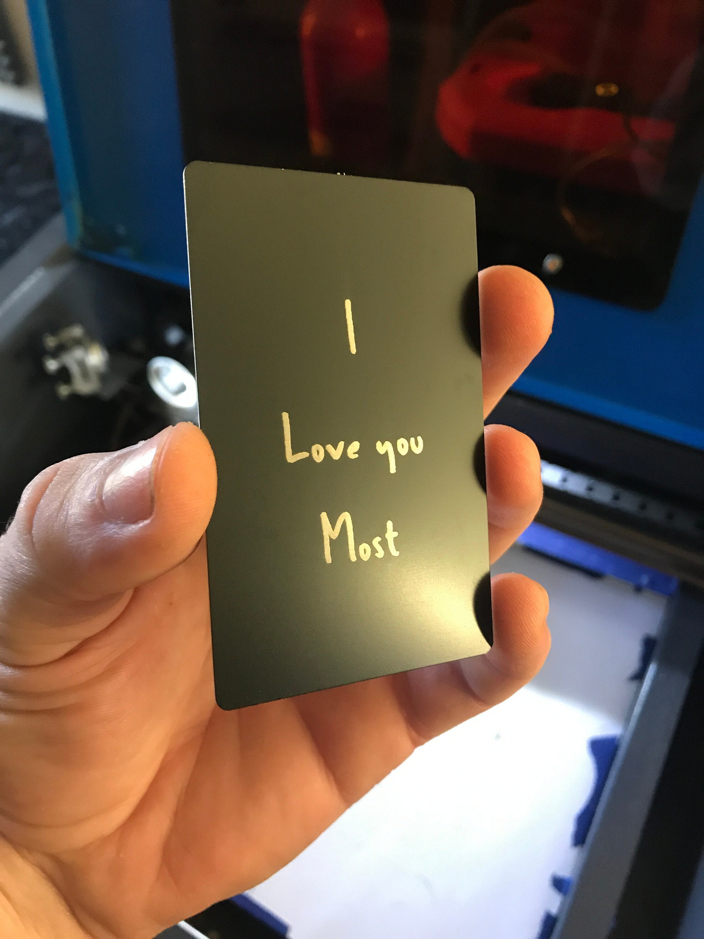 Hand holding a black/silver metal gift card with 'I Love you Most' text against a blurred background