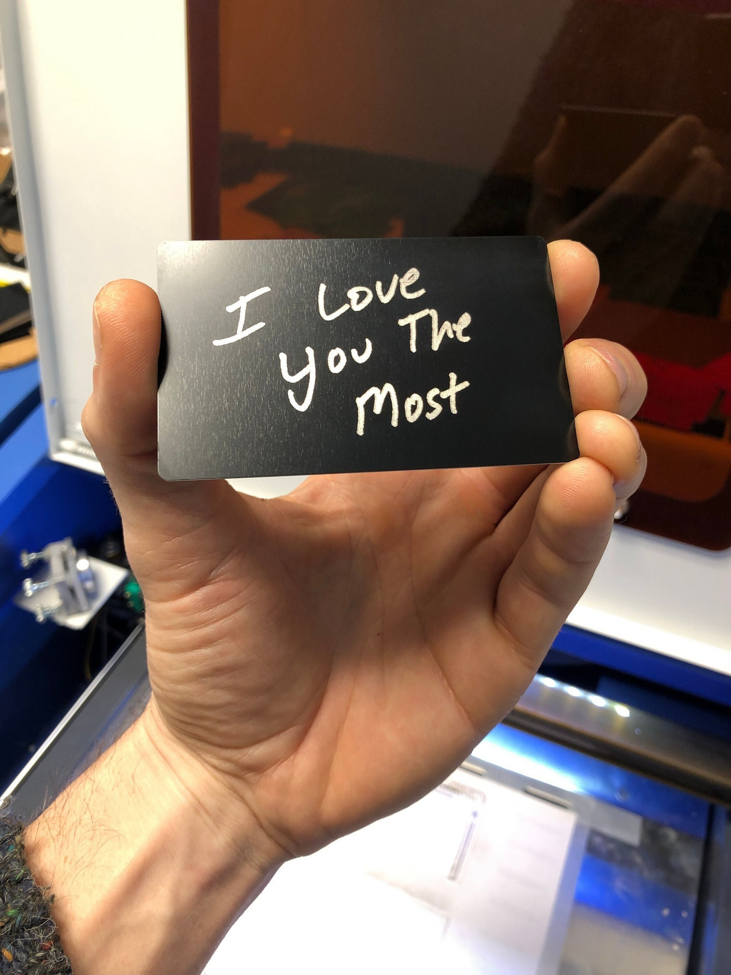Hand holding a black metal keepsake card with 'I Love You The Most' engraving.