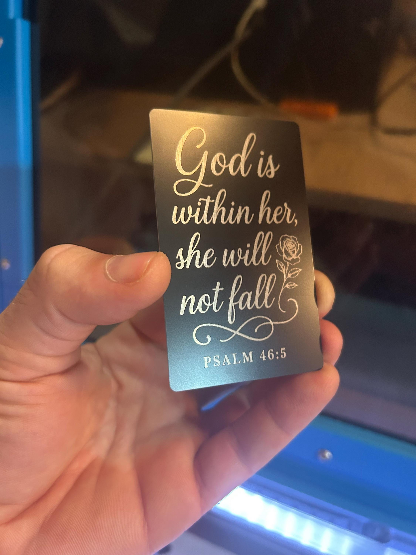 Hand holding laser engraved metal keepsake bookmark card, with Psalm 46:5 inscription and rose image
