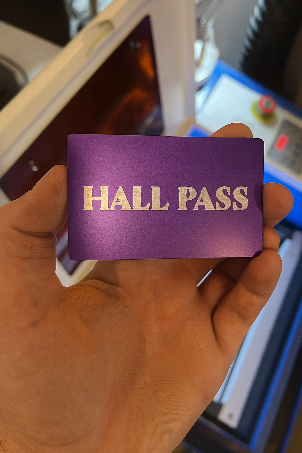 Hand holding a purple/silver 'Hall Pass' card with a blurred background