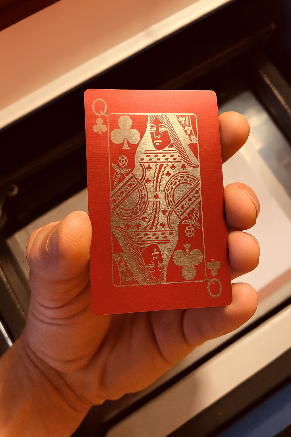 Hand holding a red/silver metal poker cards with a laser engraved queen design