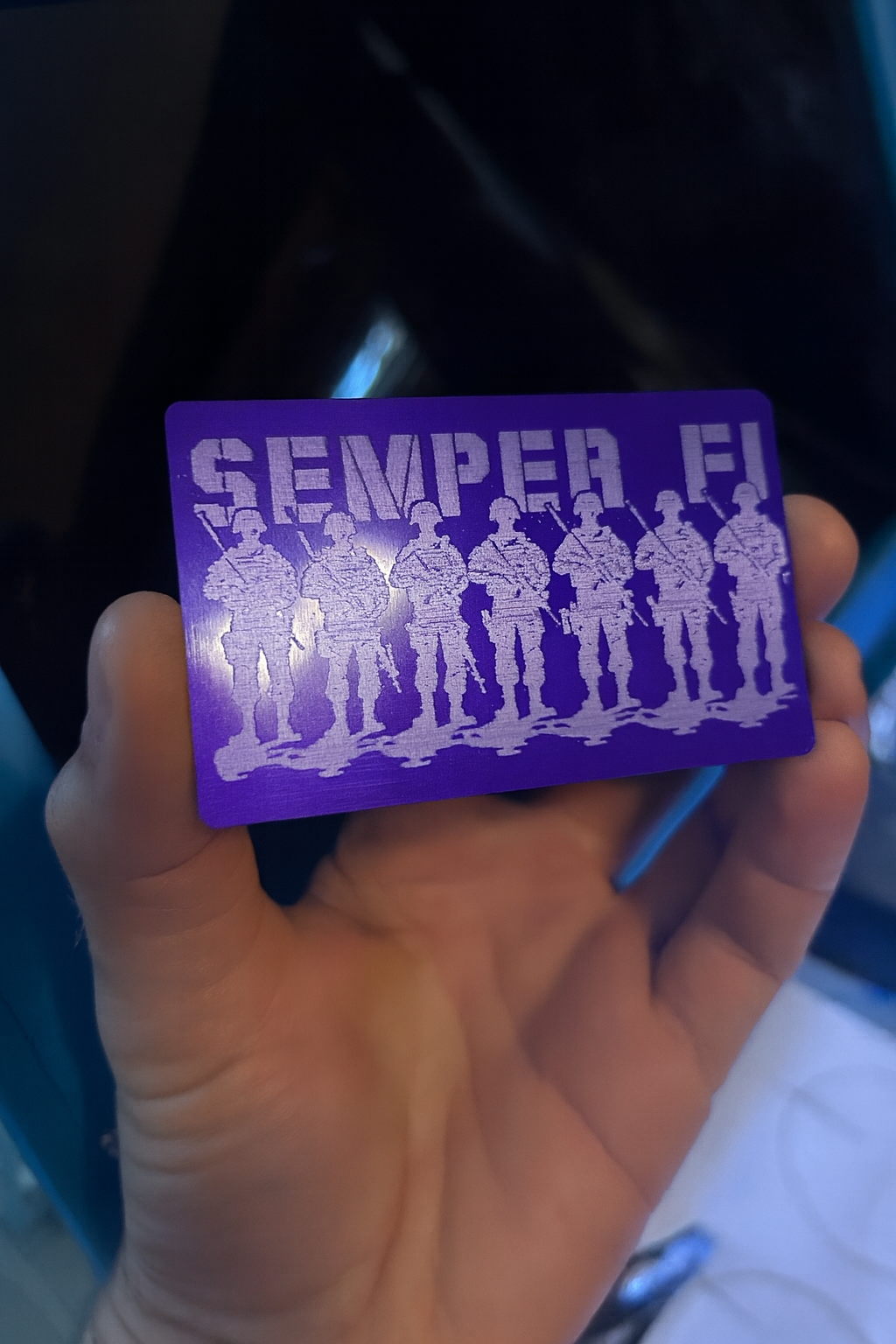 Purple/silver metal card with white 'Semper Fi' design held by a hand