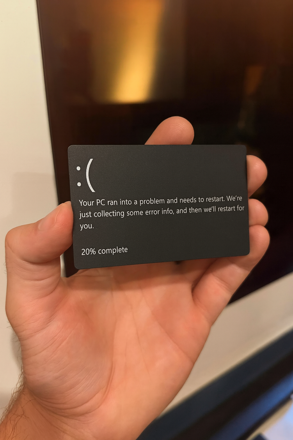 Hand holding a metal black/silver card with blue screen of death text on it against a blurred background