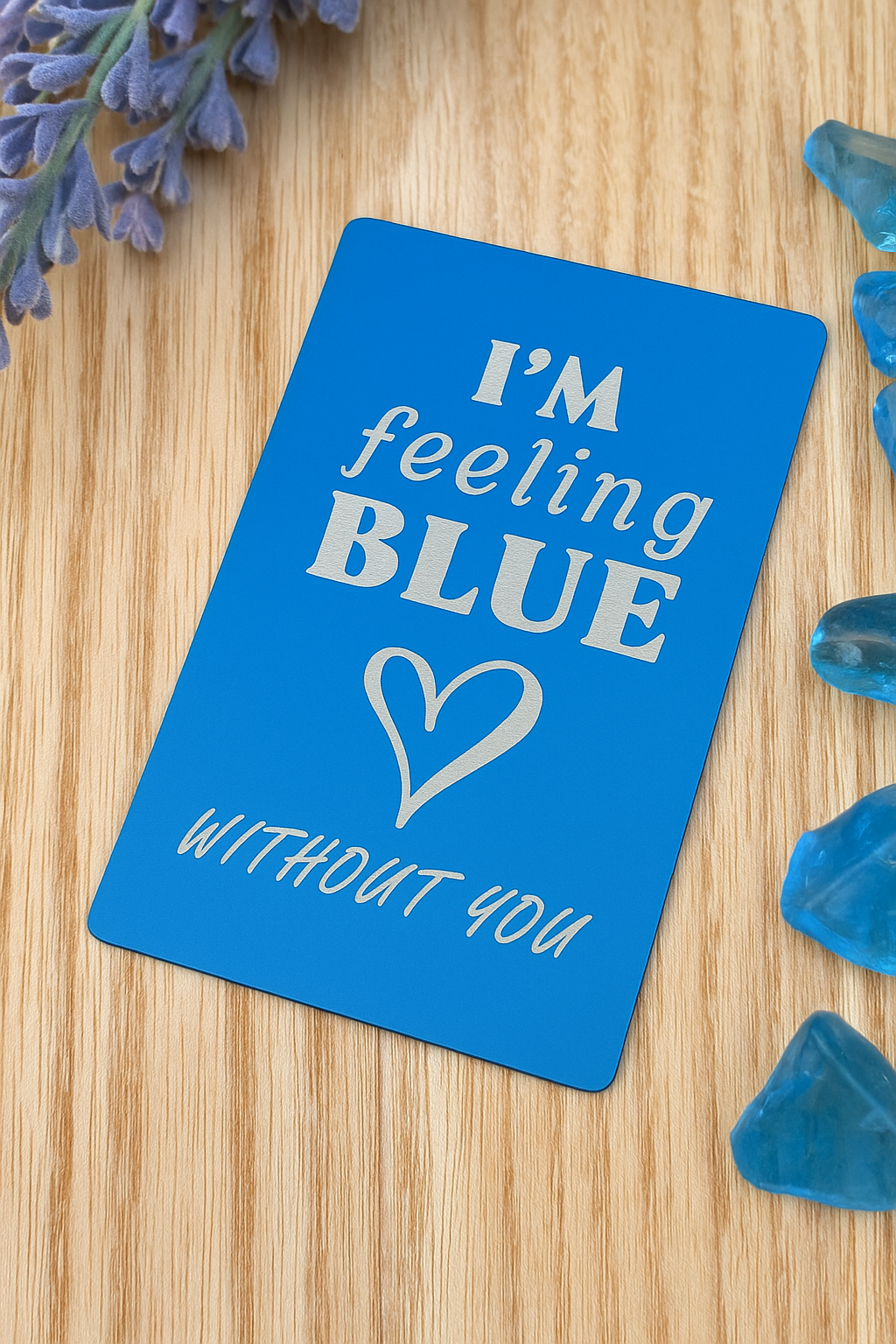 Blue/silver metal engraved romantic gift card with 'I'm feeling BLUE without you' text on a wooden surface with blue decorative elements.