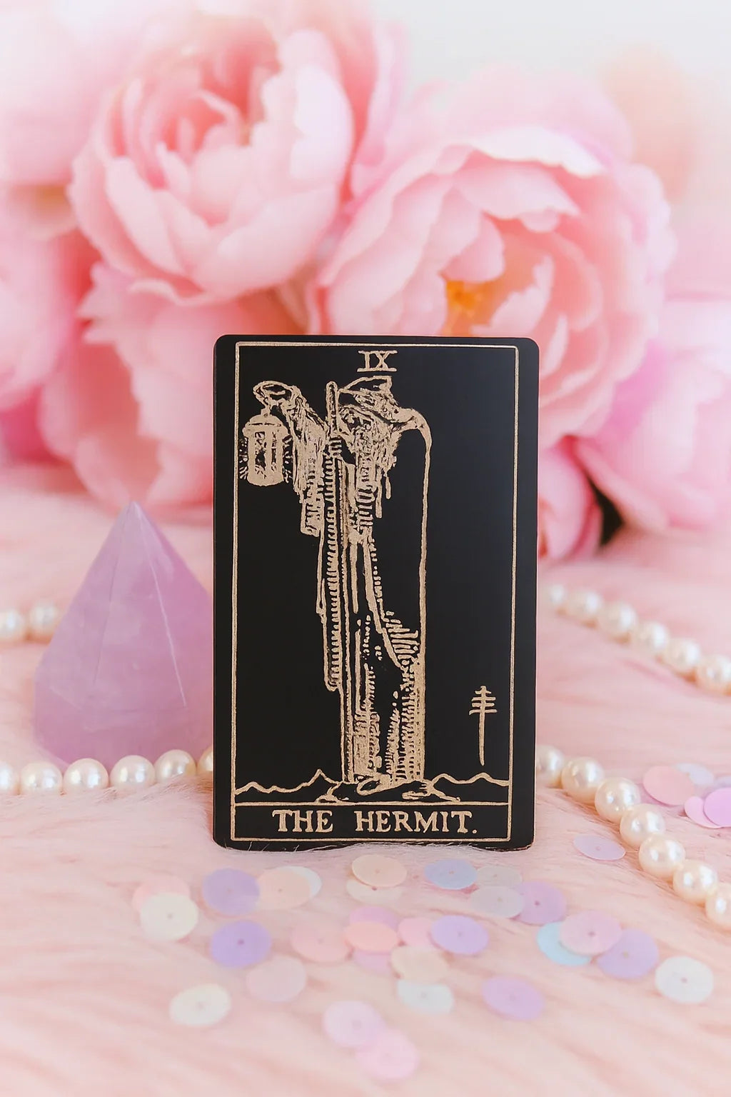 Metal Tarot card titled 'The Hermit' with pink flowers and pearls in the background