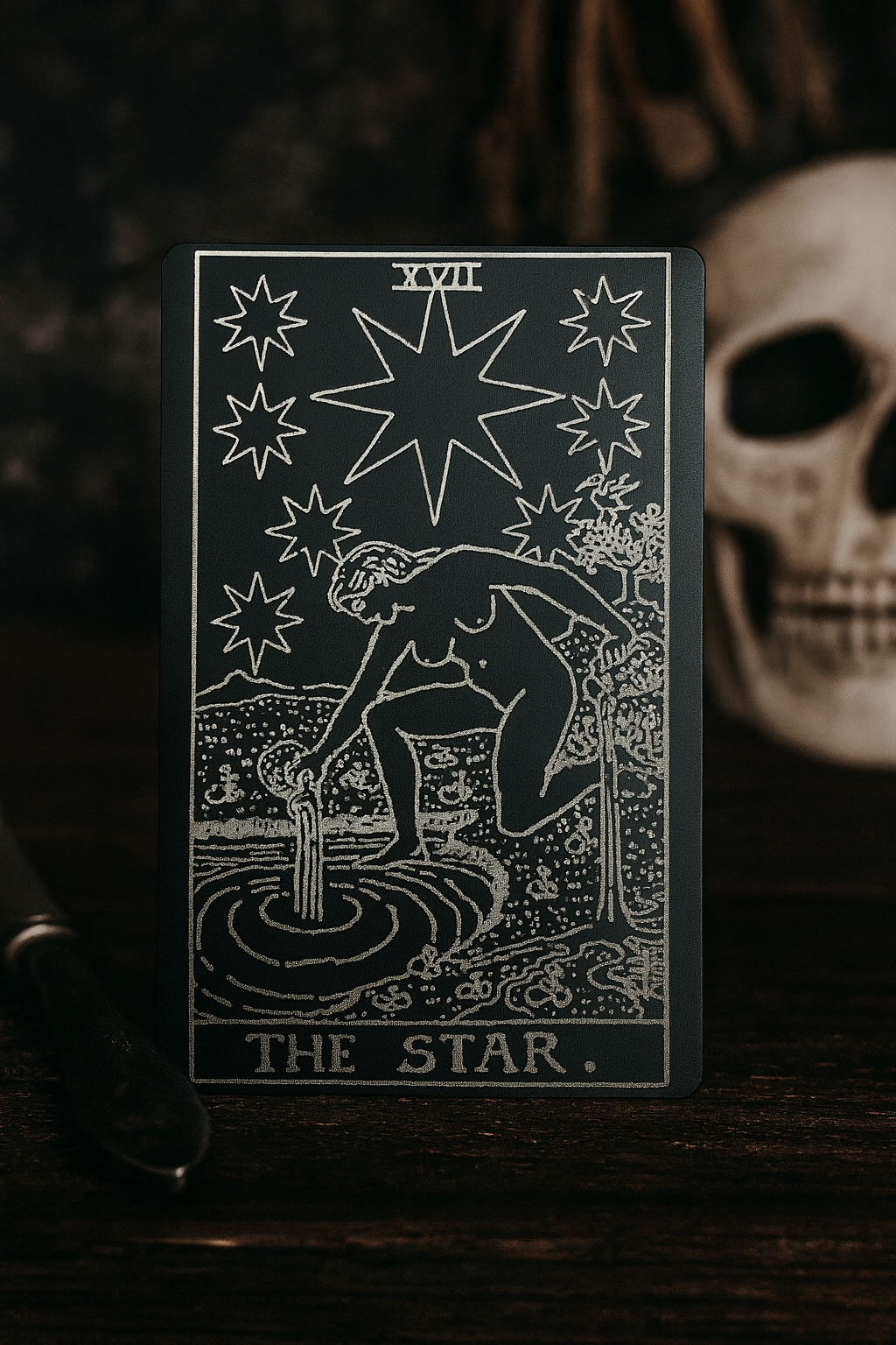 Tarot card laser engraved in matte black anodized aluminum of 'The Star' with star design and person at a well, on a dark background.