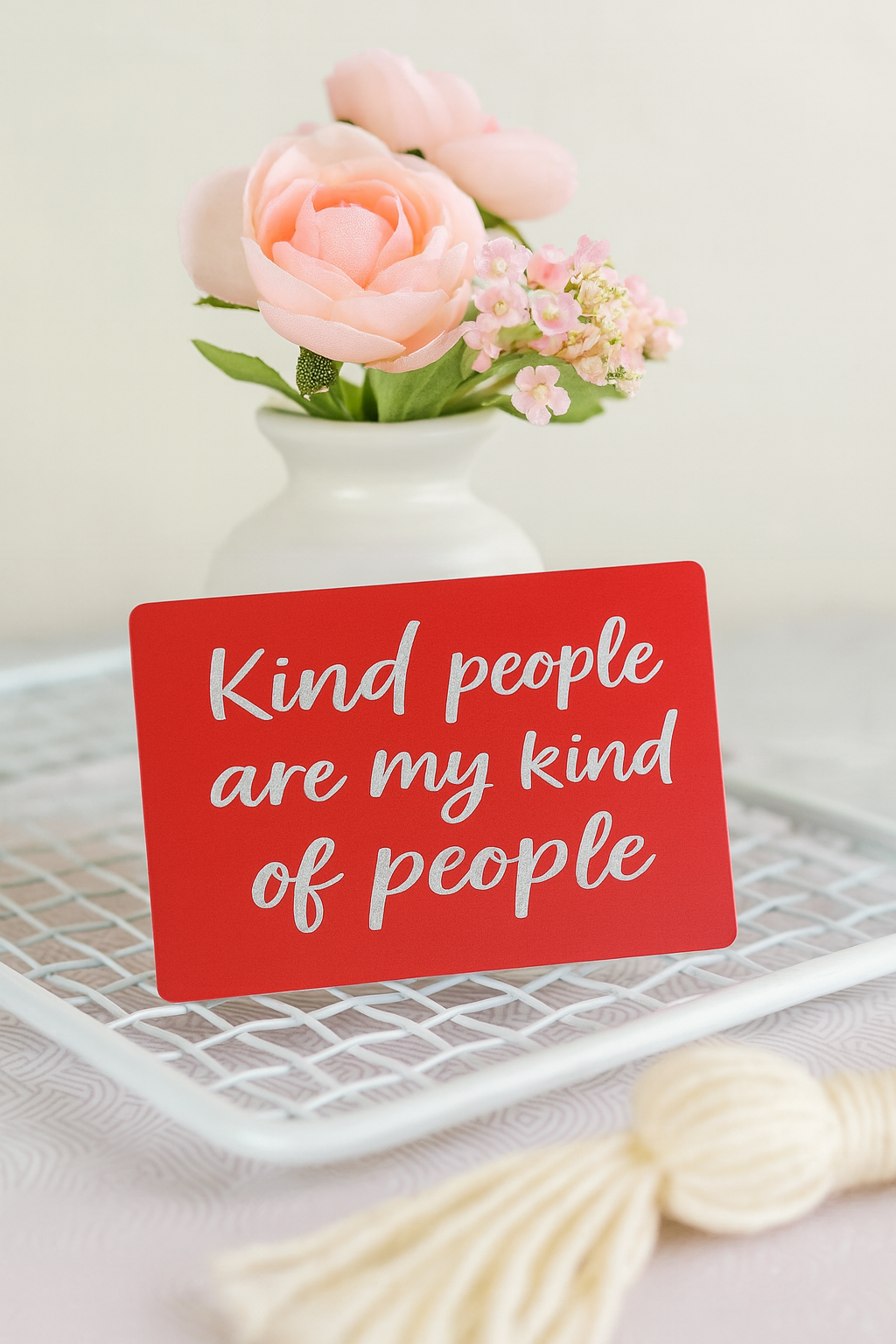 Red/silver metal laser engraved card with 'Kind people are my kind of people' text, placed on a white surface with flowers and a decorative item.