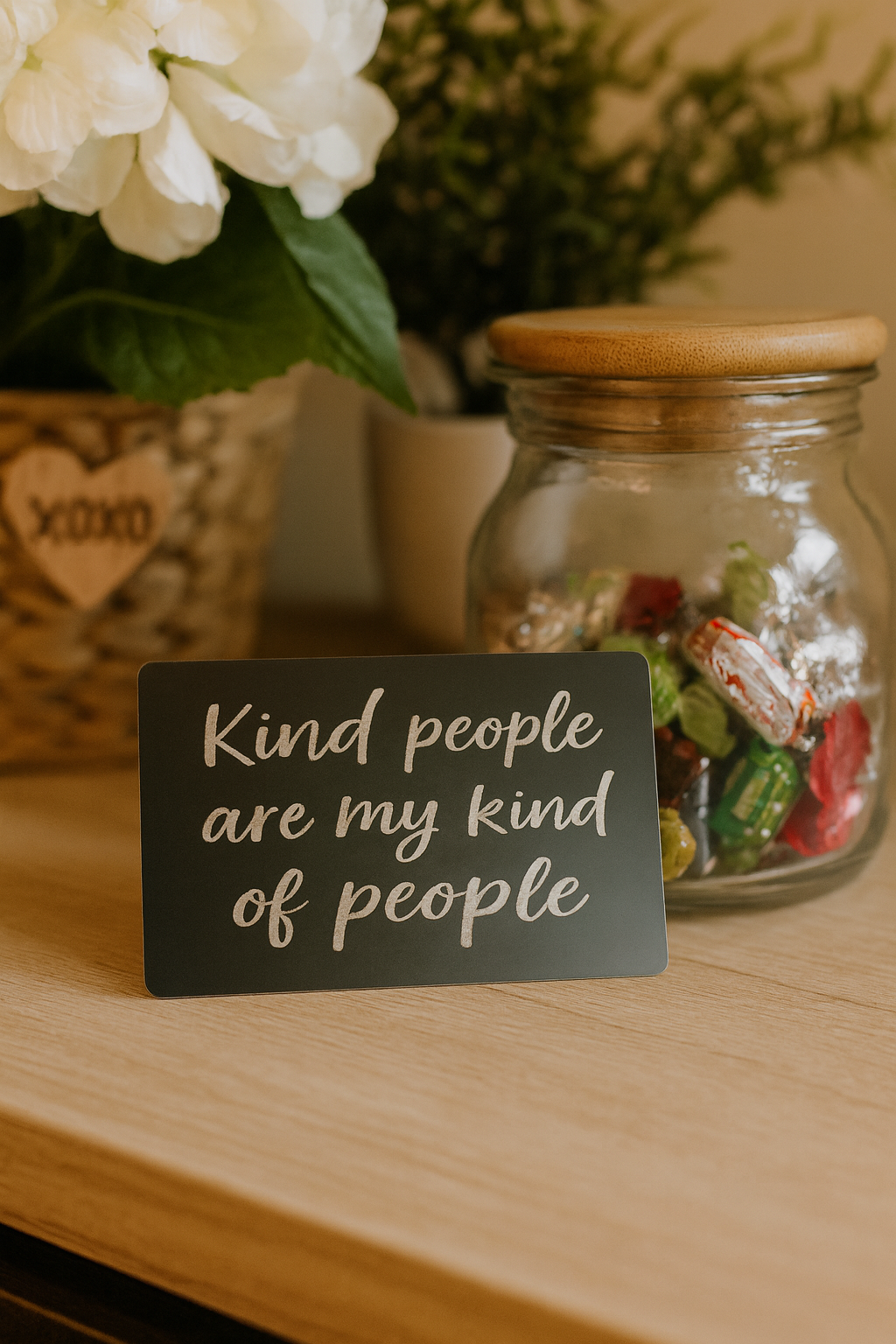 Jar of candies with a metal placard sign reading 'Kind people are my kind of people' on a wooden surface.