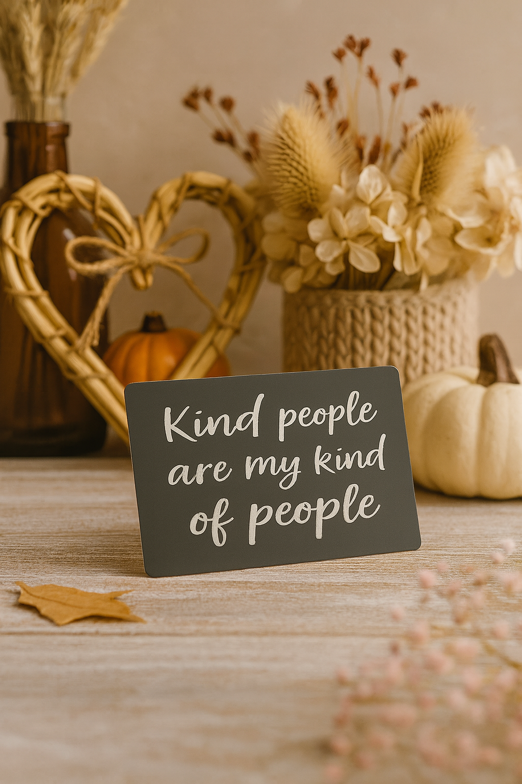 Decorative metal sign with 'Kind people are my kind of people' text on a table with autumn decorations.