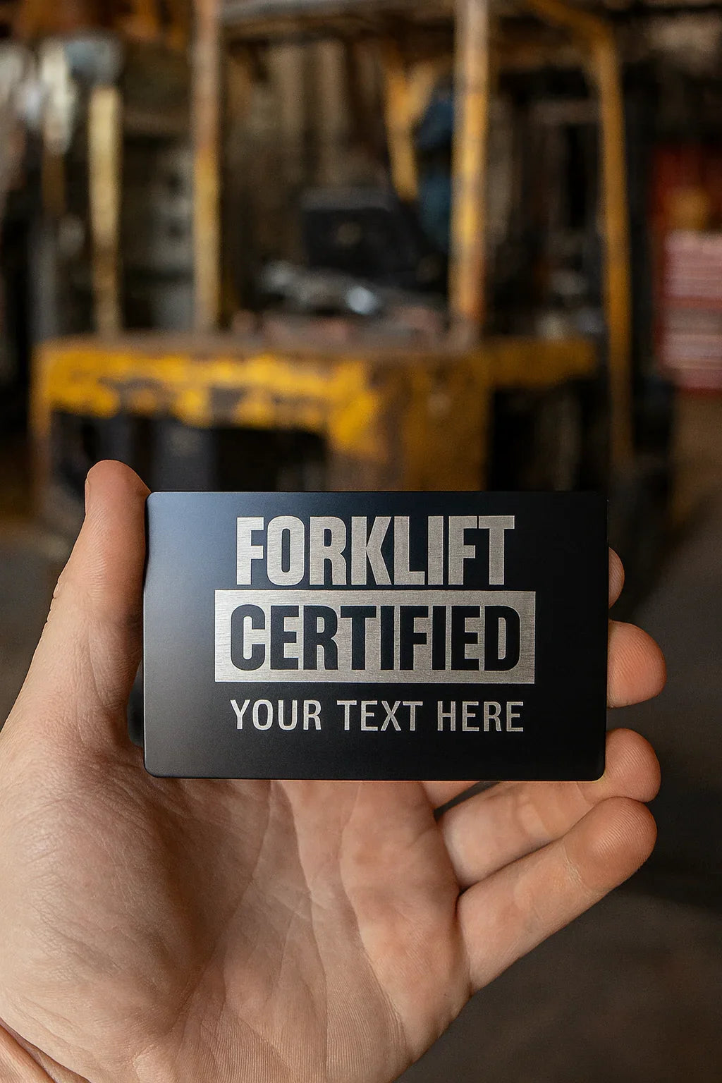 Hand holding a 'Forklift Certified' card with a forklift in the background
