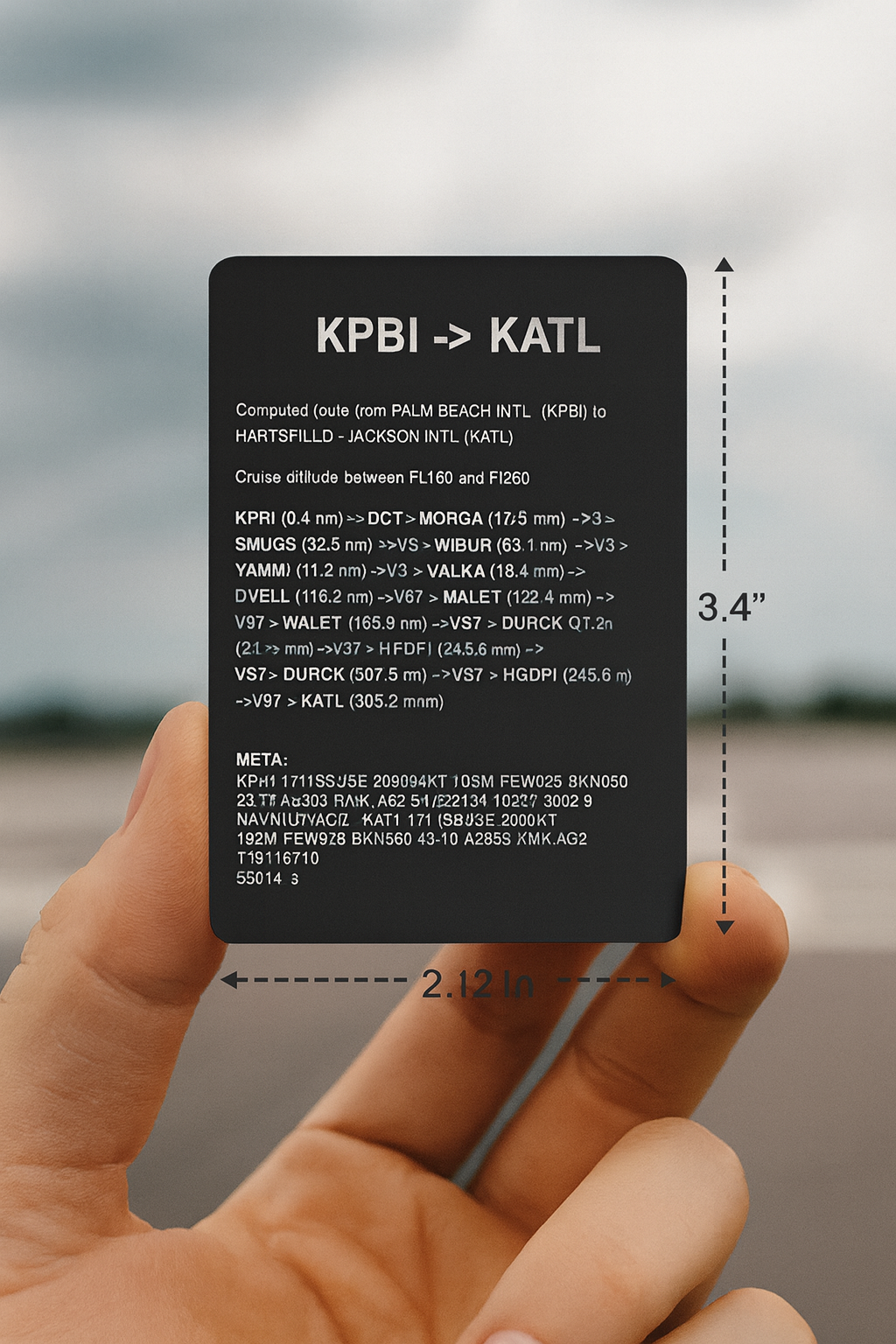 Hand holding a small black card with flight plan engraving set against a blurred airport background.