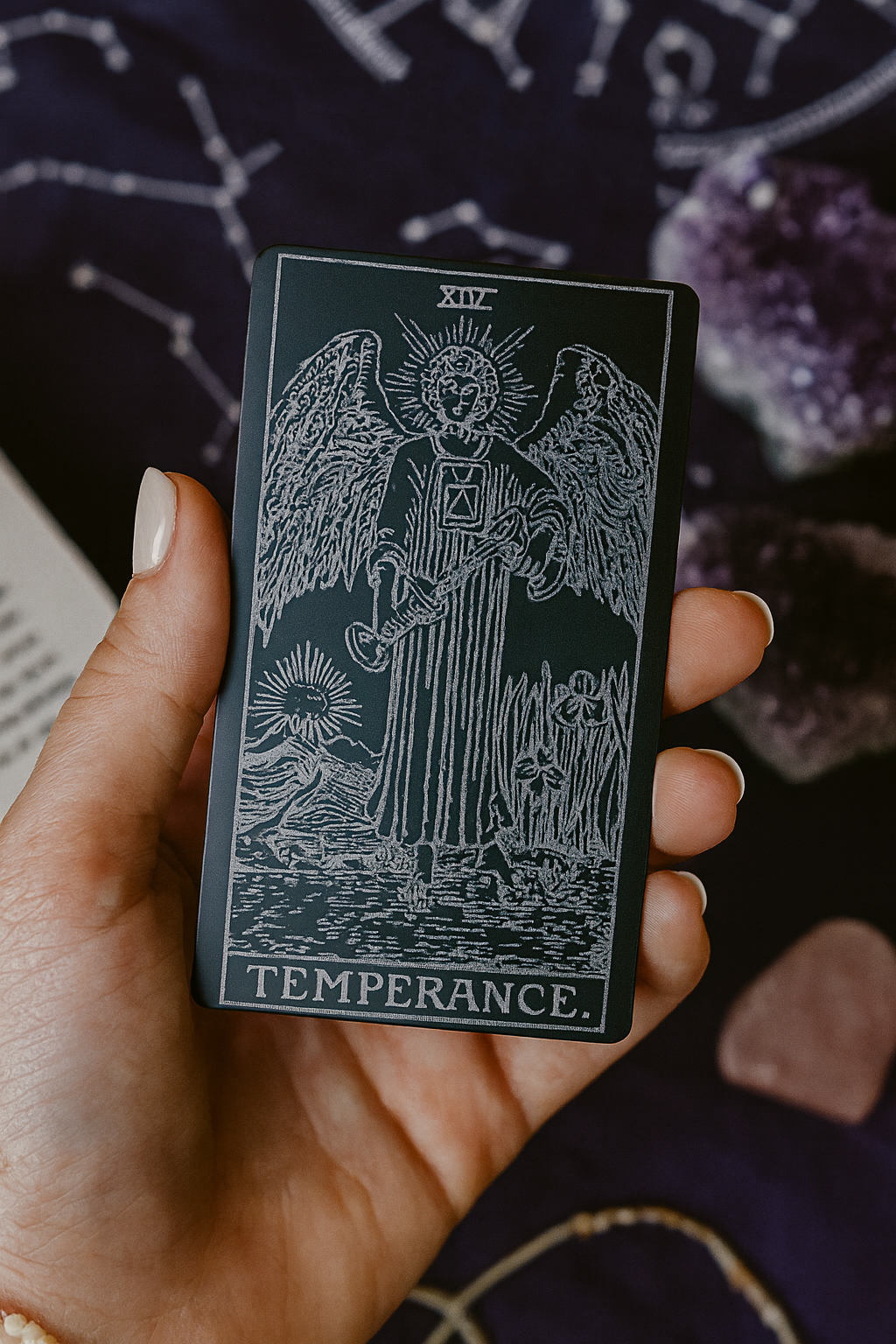 Hand holding a tarot card titled 'Temperance' with intricate design on a dark background.