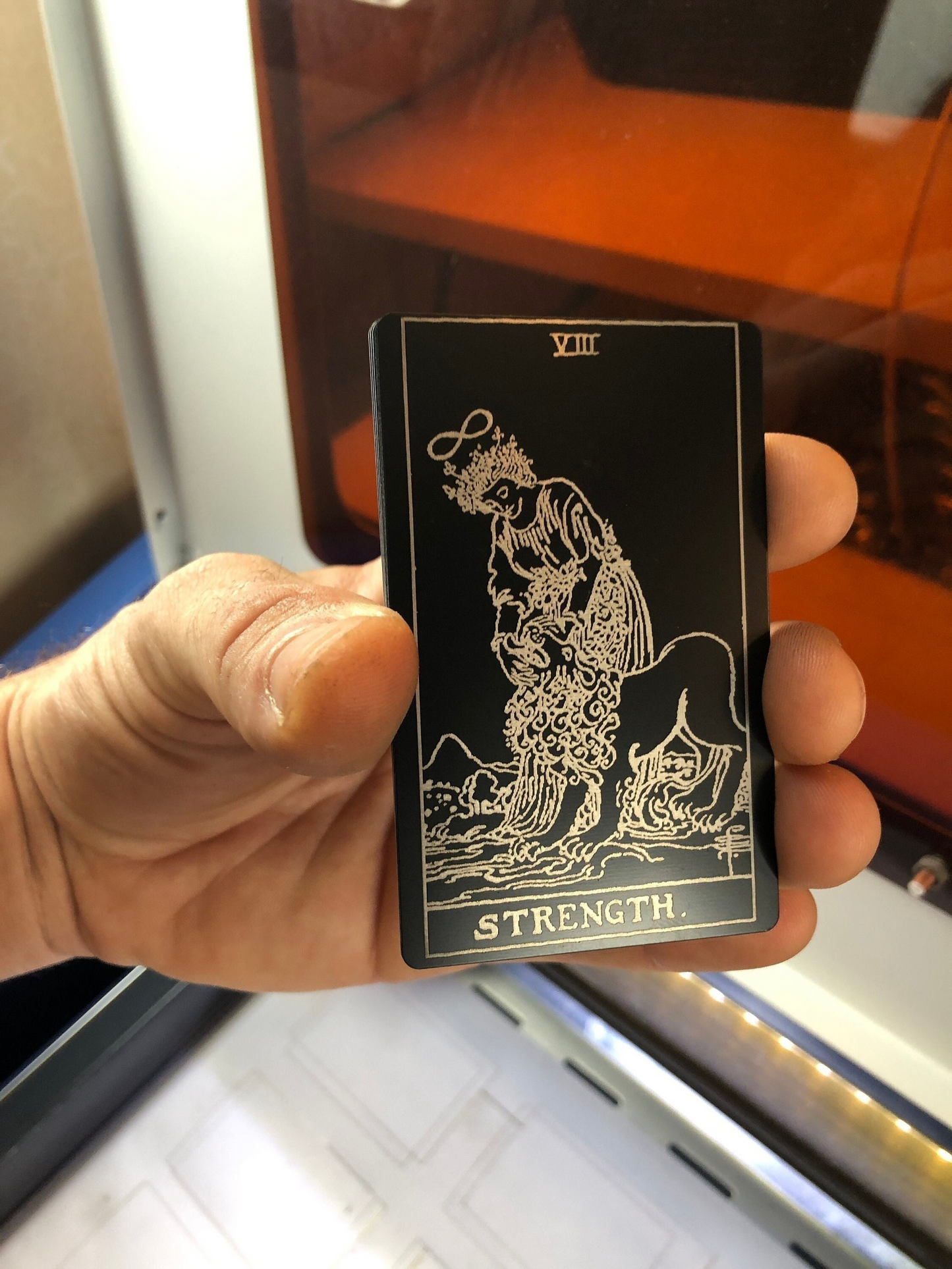 Hand holding a metal tarot card with 'Strength' symbol
