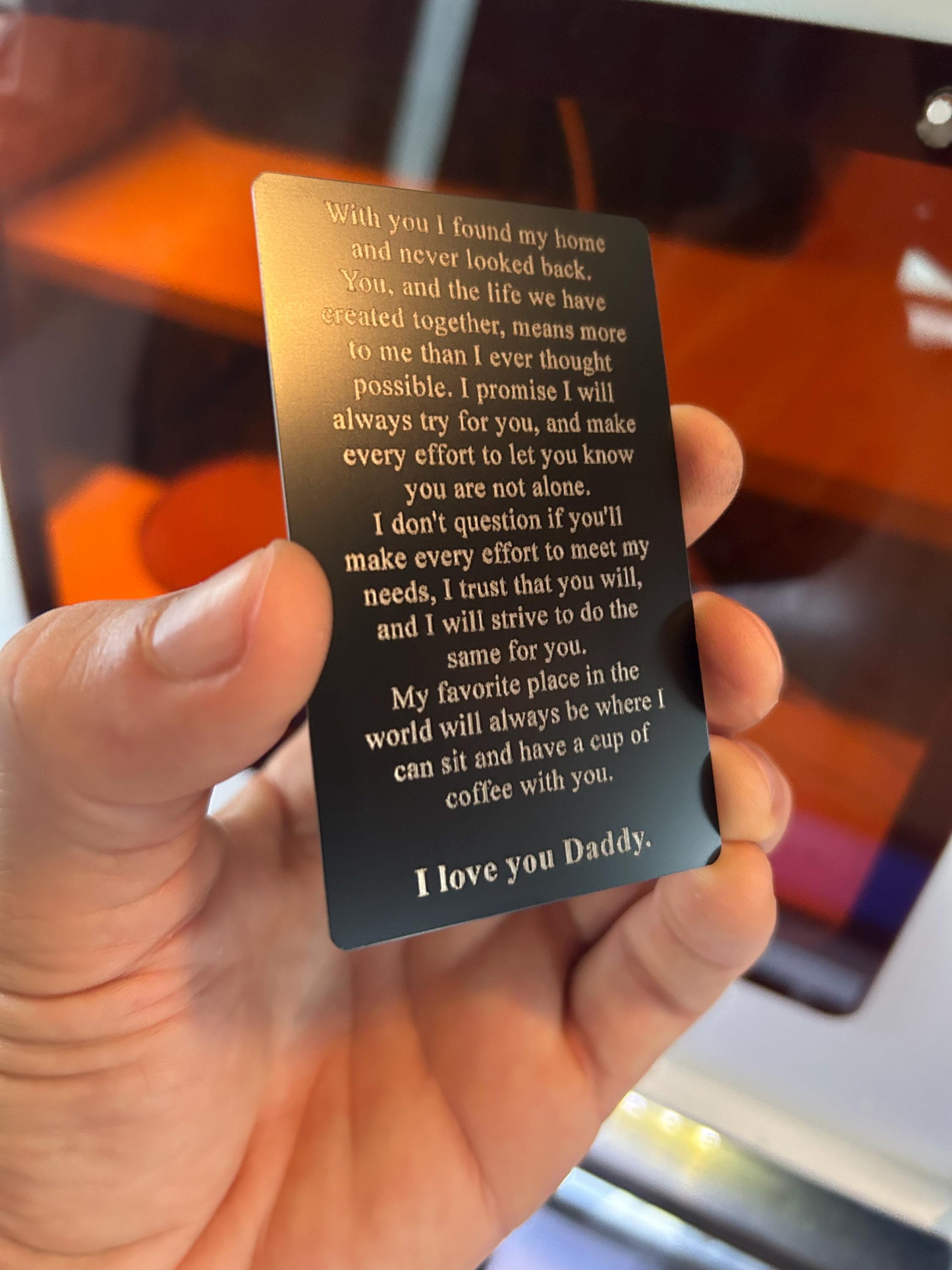Hand holding a silver metal laser engraved gift card with a heartfelt message in front of a blurred background