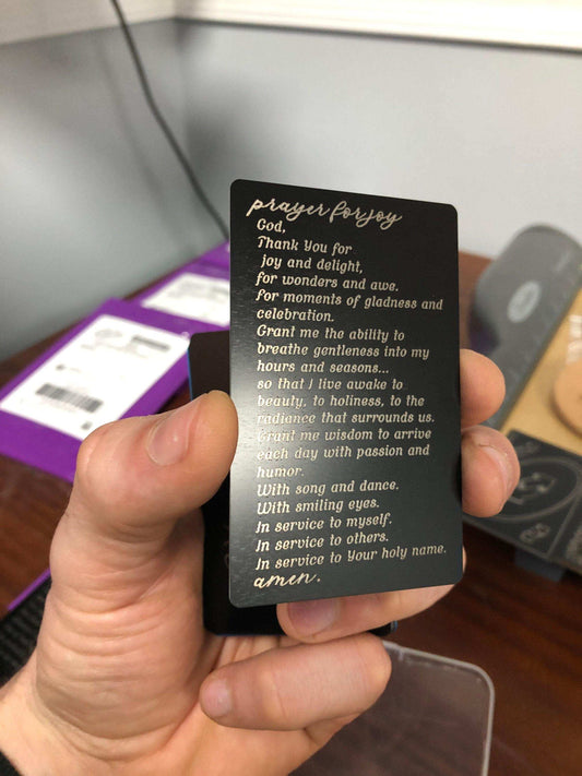 Hand holding a matte black prayer card with laser engraved silver text.