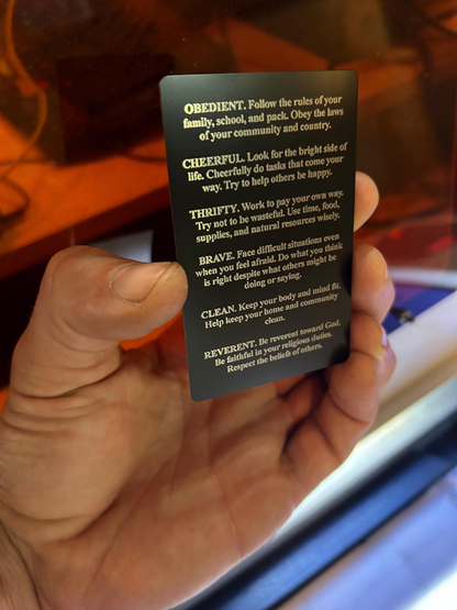 Hand holding a black card with 12 points of scout law, reverse side on a blurred background