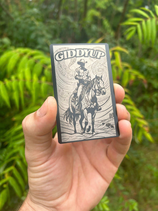 Hand holding a small rectangular wallet insert with 'Giddy Up' cowboy art against a green background