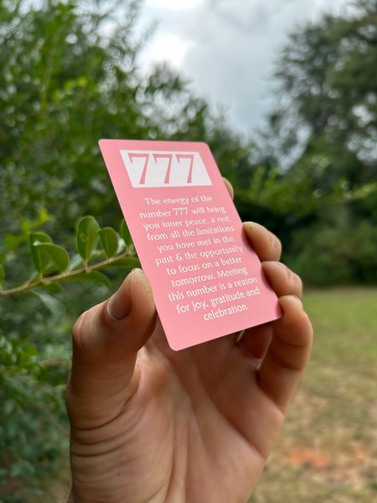 Hand holding a pink card with '777' and text against a blurred green outdoor background